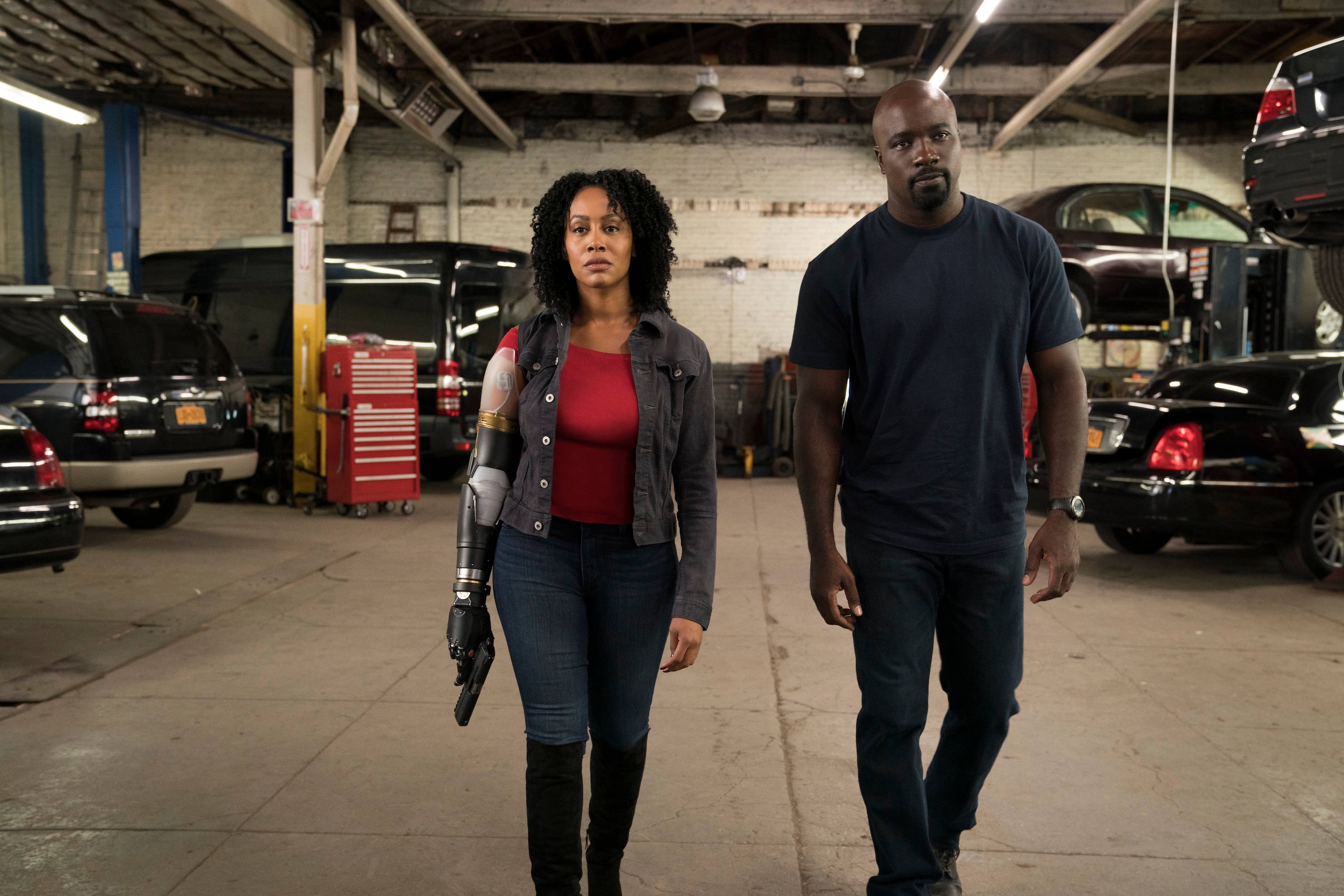 Netflix 桌布 壁紙 — 兩個堅定的人穿過一個雜亂的汽車修理廠，周圍有汽車和工具。