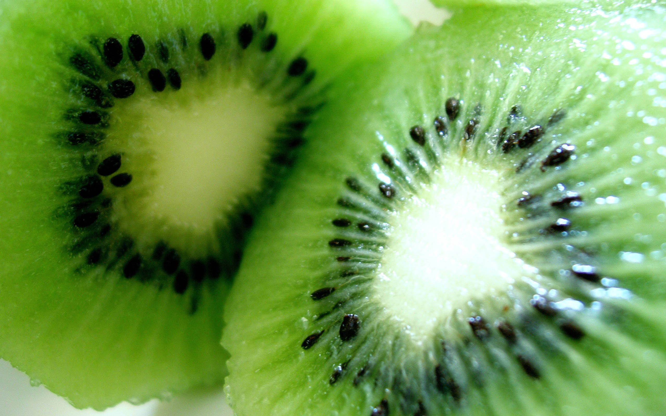 Kiwi 桌布 壁紙 — 兩個多汁奇異果半邊的特寫，展現出充滿活力的綠色果肉和黑色種子。