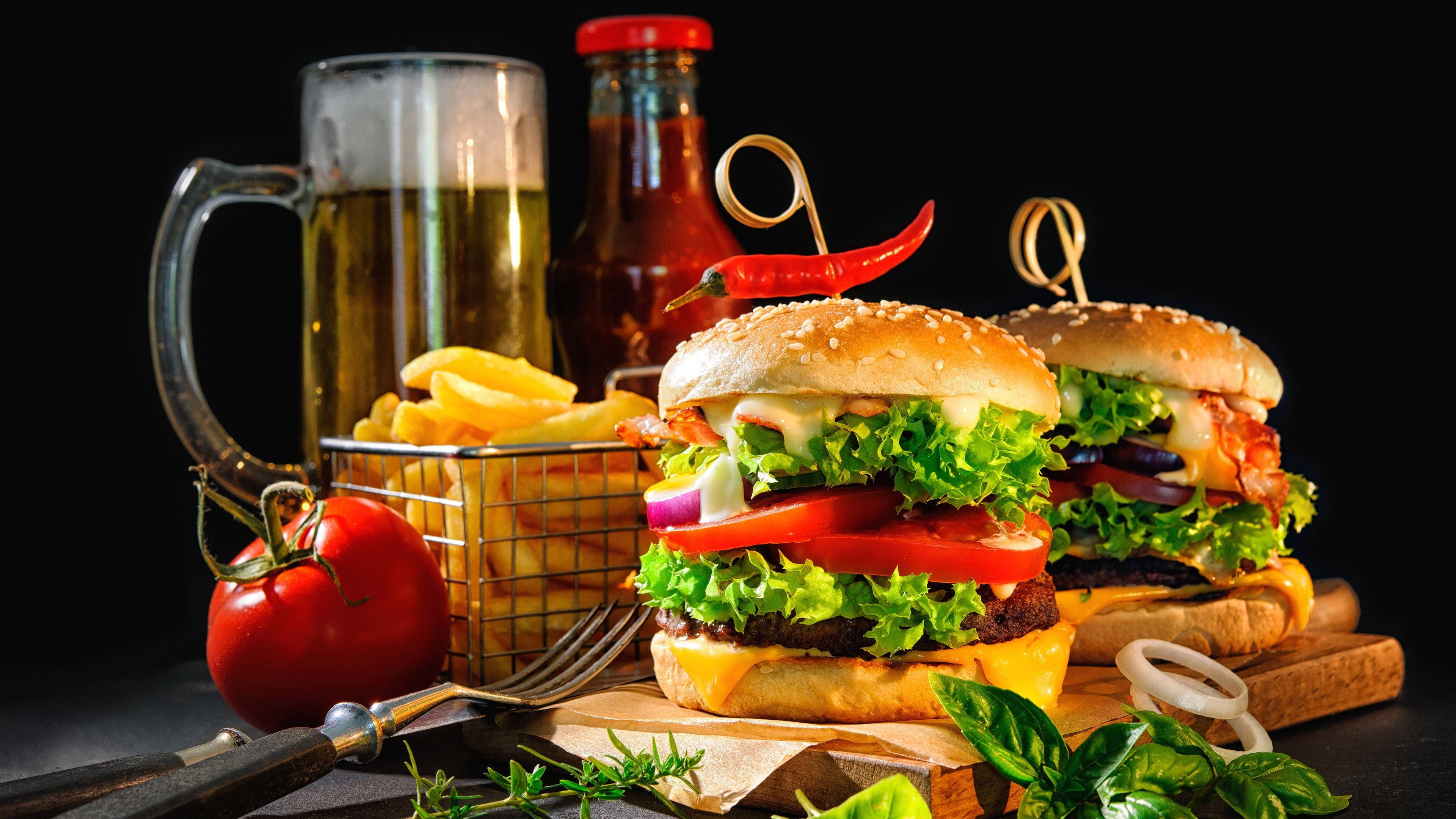 Food Photography 桌布 壁紙 — 兩個多汁漢堡，搭配新鮮生菜、番茄和起司，放在木板上，旁邊有薯條、啤酒和紅辣椒，背景為黑色。