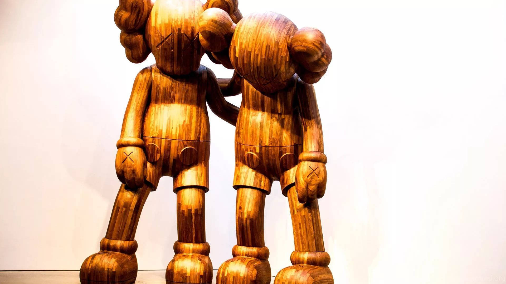 kaws pc 桌布 壁紙 — 兩個大型木製KAWS公仔在畫廊環境中，靠著純白牆壁互相擁抱。