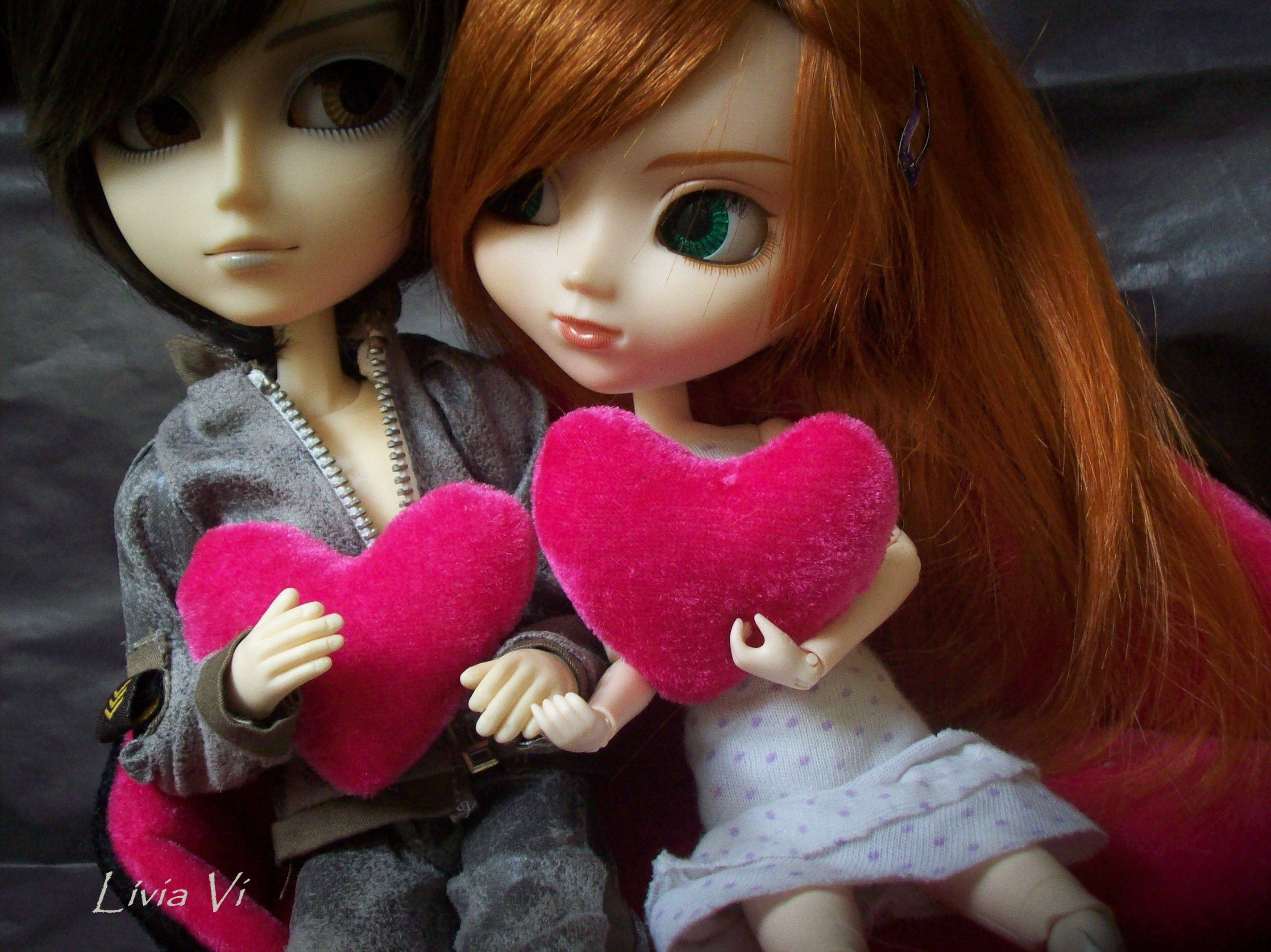 cute doll couple 桌布 壁紙 — 兩個大眼睛的動漫風格玩偶緊挨著坐在一起，在深色紋理背景前手持亮粉紅色絨毛心形。