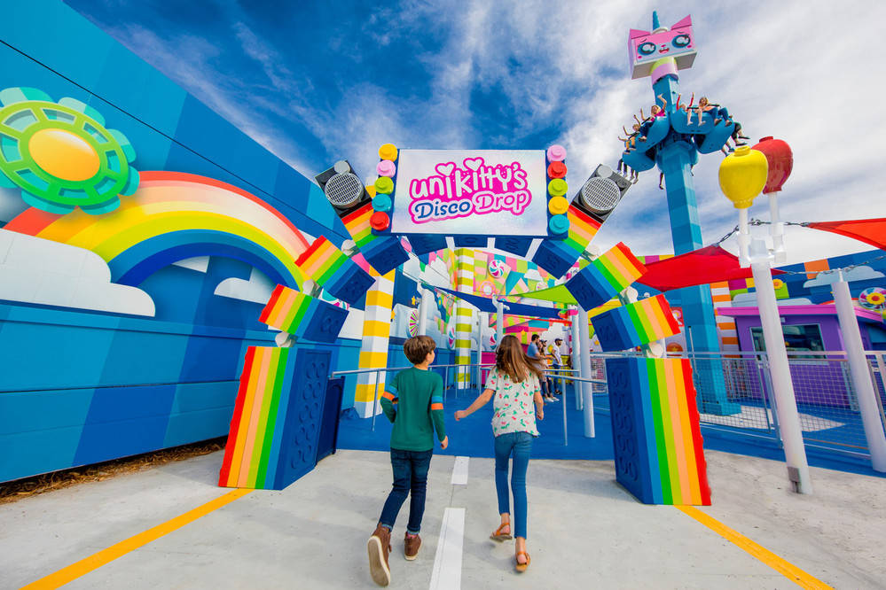 Legoland 桌布 壁紙 — 兩個孩子在明亮的藍天下走向Unikitty's Disco Drop遊樂設施的鮮豔彩虹主題入口。
