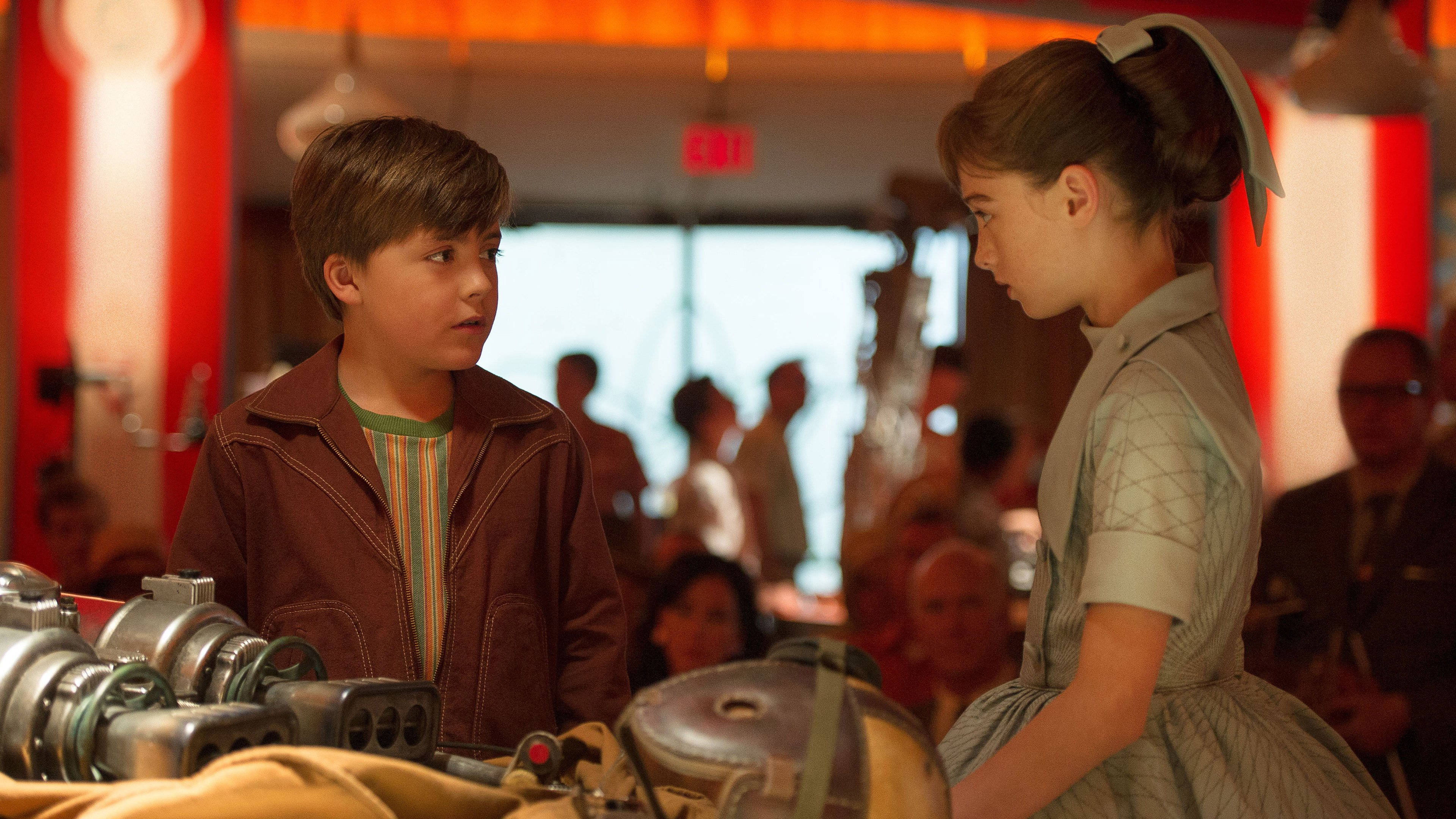 Tomorrowland Movie 桌布 壁紙 — 兩個孩子在燈光溫暖的餐廳裡，在一張堆滿復古機器的桌子上進行嚴肅的對話。