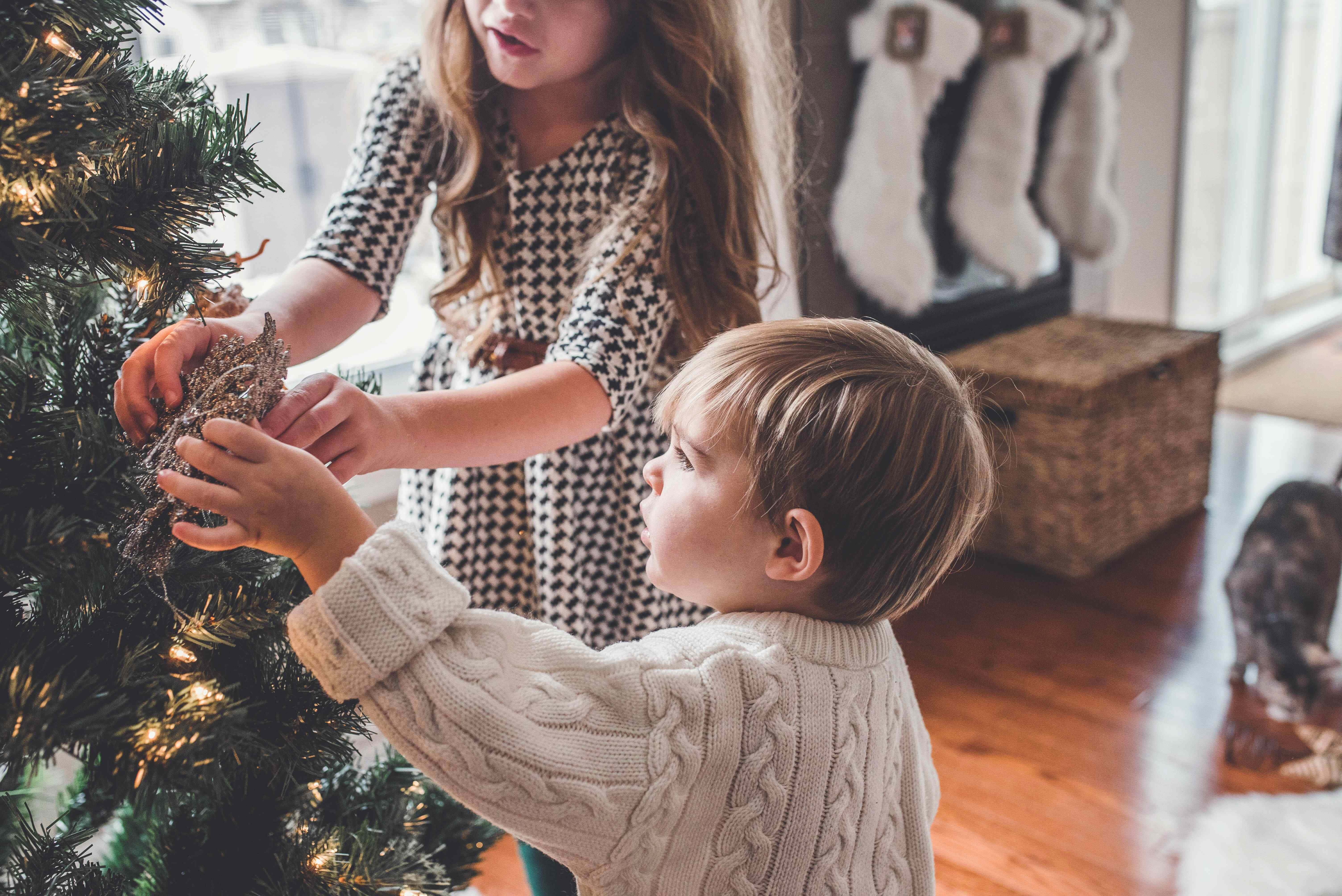Christmas Scene 桌布 壁紙 — 兩個孩子在陽光明媚的客廳裡，用舒適的針織毛衣裝飾溫暖明亮的聖誕樹。