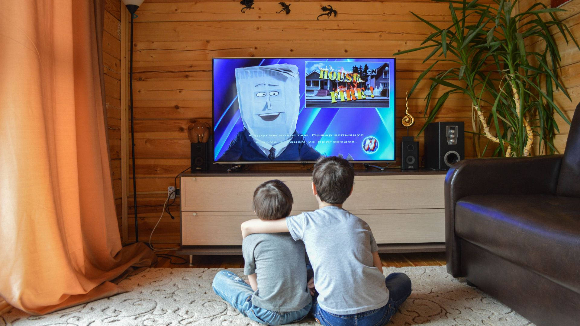 tv 桌布 壁紙 — 兩個孩子坐在舒適的木製客廳地毯上，看著電視上的動畫節目。