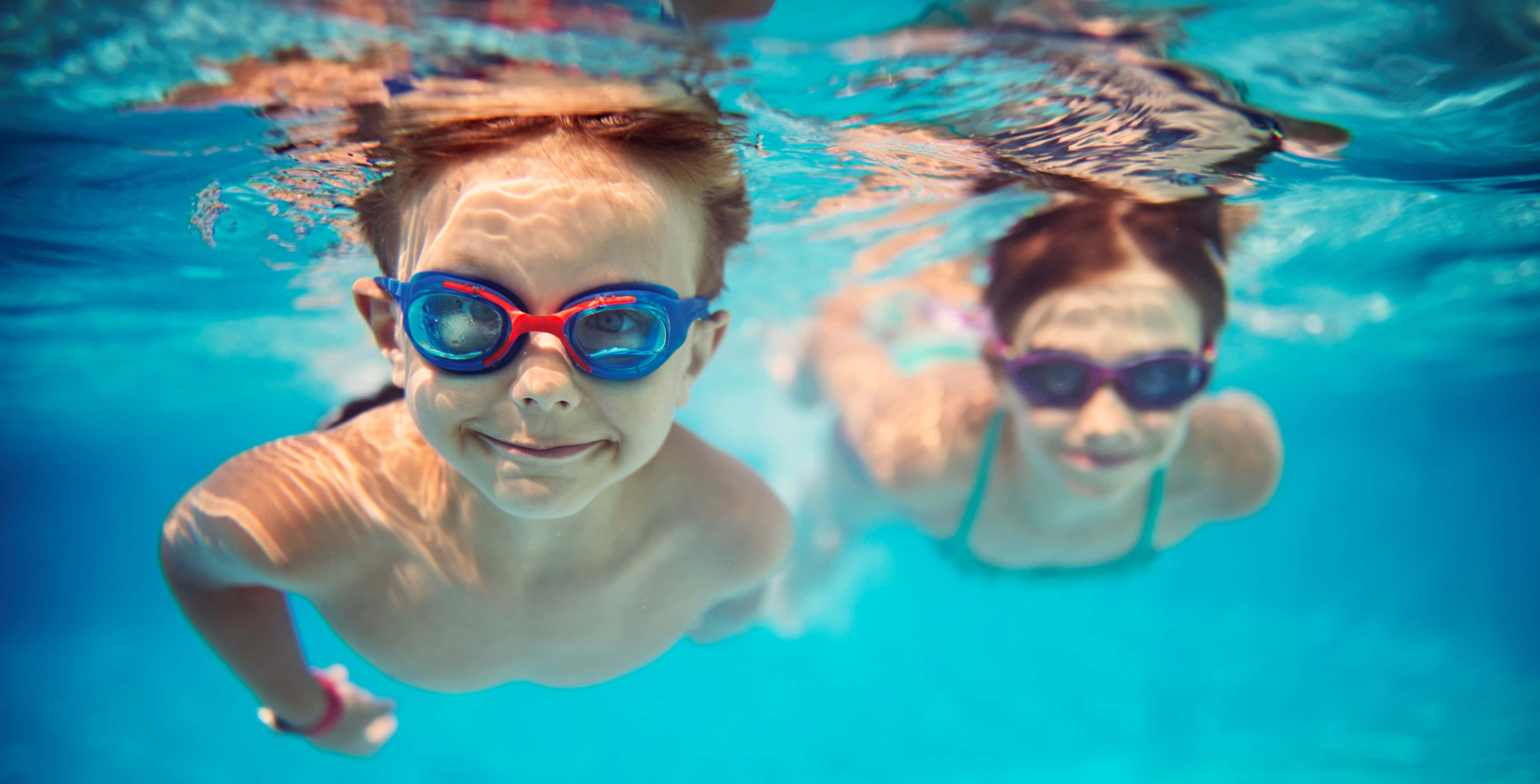 Swimming 桌布 壁紙 — 兩個孩子戴著彩色泳鏡在泳池中水下游泳，表情歡樂。