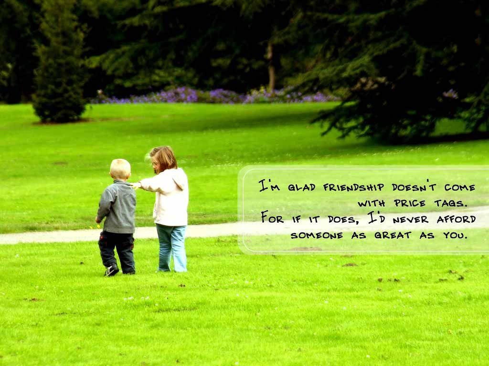 Friendship Quotes 桌布 壁紙 — 兩個孩子手牽手走過一片充滿活力的綠色草坪，遠處是帶有紫色花朵的樹冠。