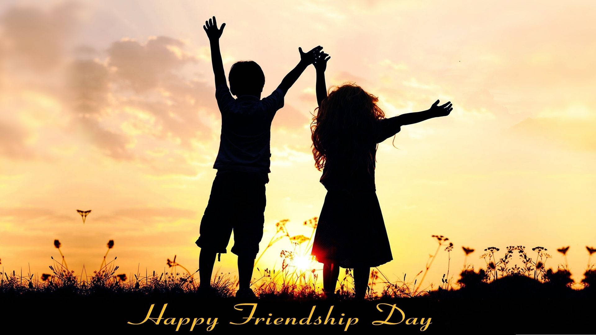 Friendship Day 桌布 壁紙 — 兩個孩子的剪影映襯著金色日落，在長滿青草的山丘上歡樂地舉起雙臂。