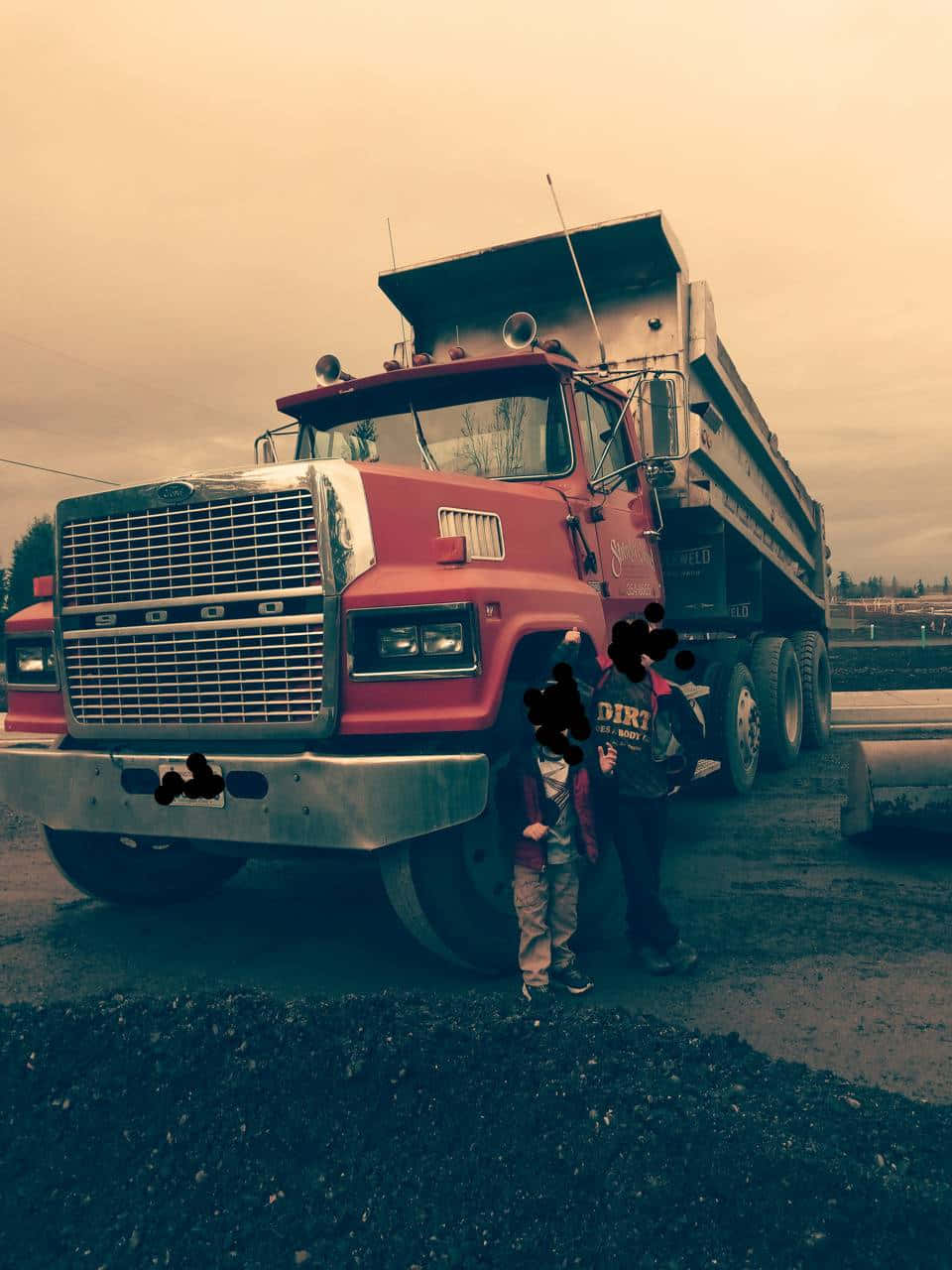 Dump Truck 桌布 壁紙 — 兩個孩子站在一輛巨大的紅色自卸車旁，天空陰霾多雲，地面鋪滿碎石。