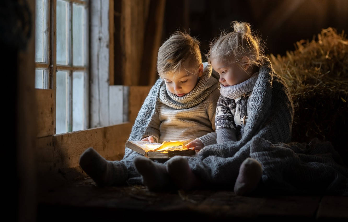 Reading 桌布 壁紙 — 兩個孩子裹著舒適的毯子，在昏暗穀倉的鄉村風格窗邊讀著一本發光的書。