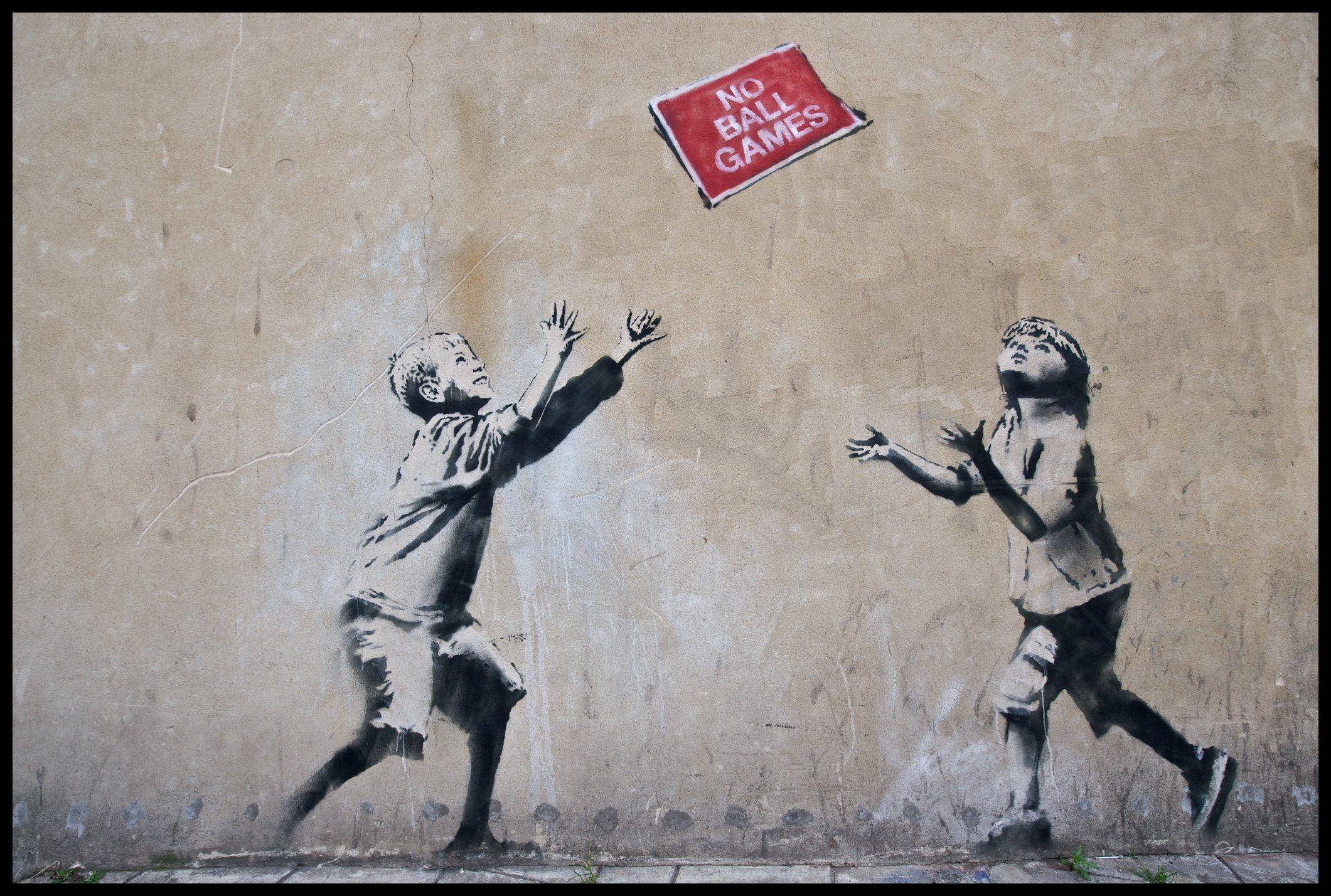 Banksy 桌布 壁紙 — 兩個孩子跳向一個漂浮的紅色標誌，上面寫著 no ball games，畫在風化的城市牆上。