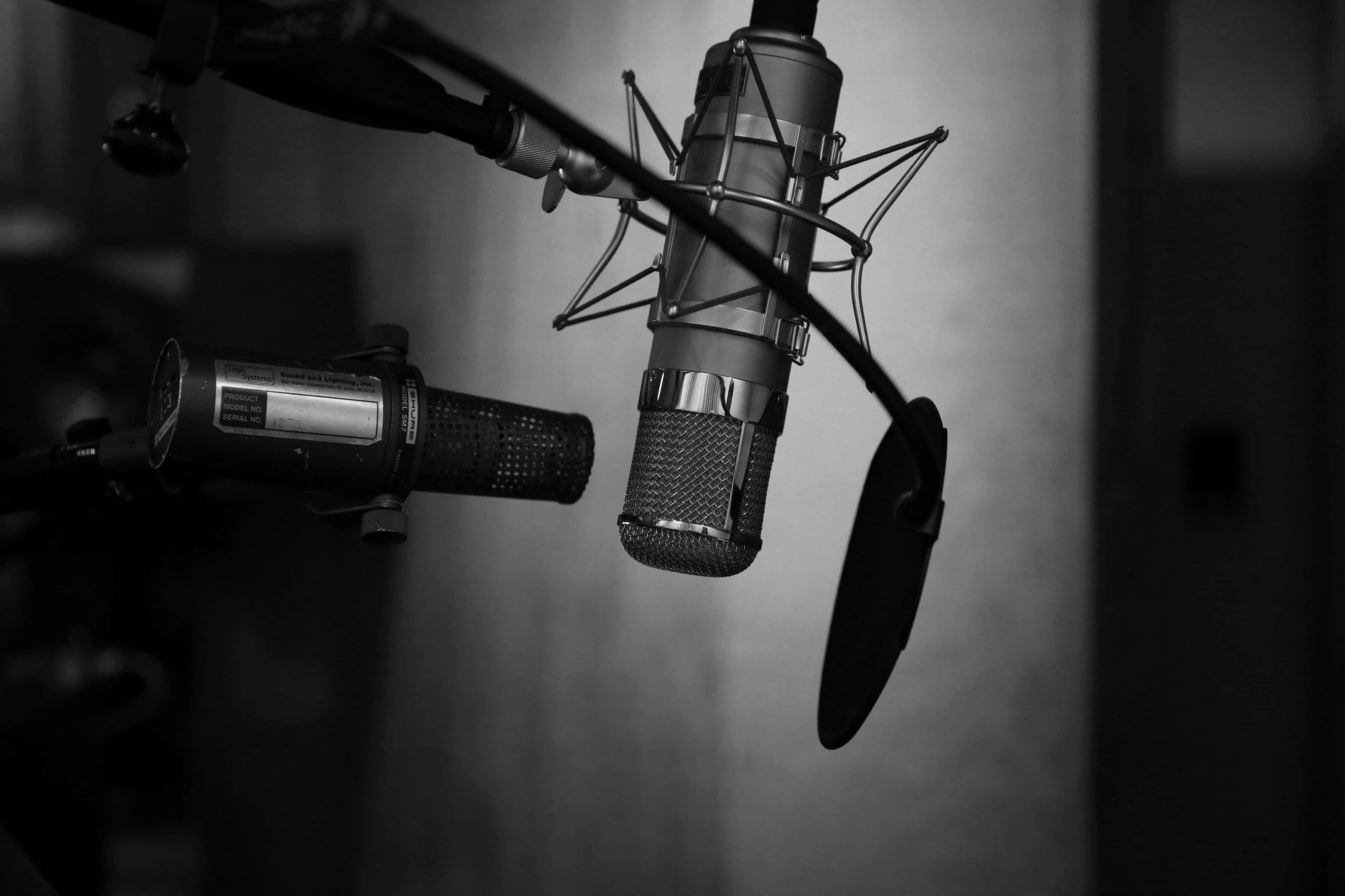 Studio 桌布 壁紙 — 兩個專業錄音室麥克風懸掛在光線昏暗的錄音室中，帶有柔和的陰影。