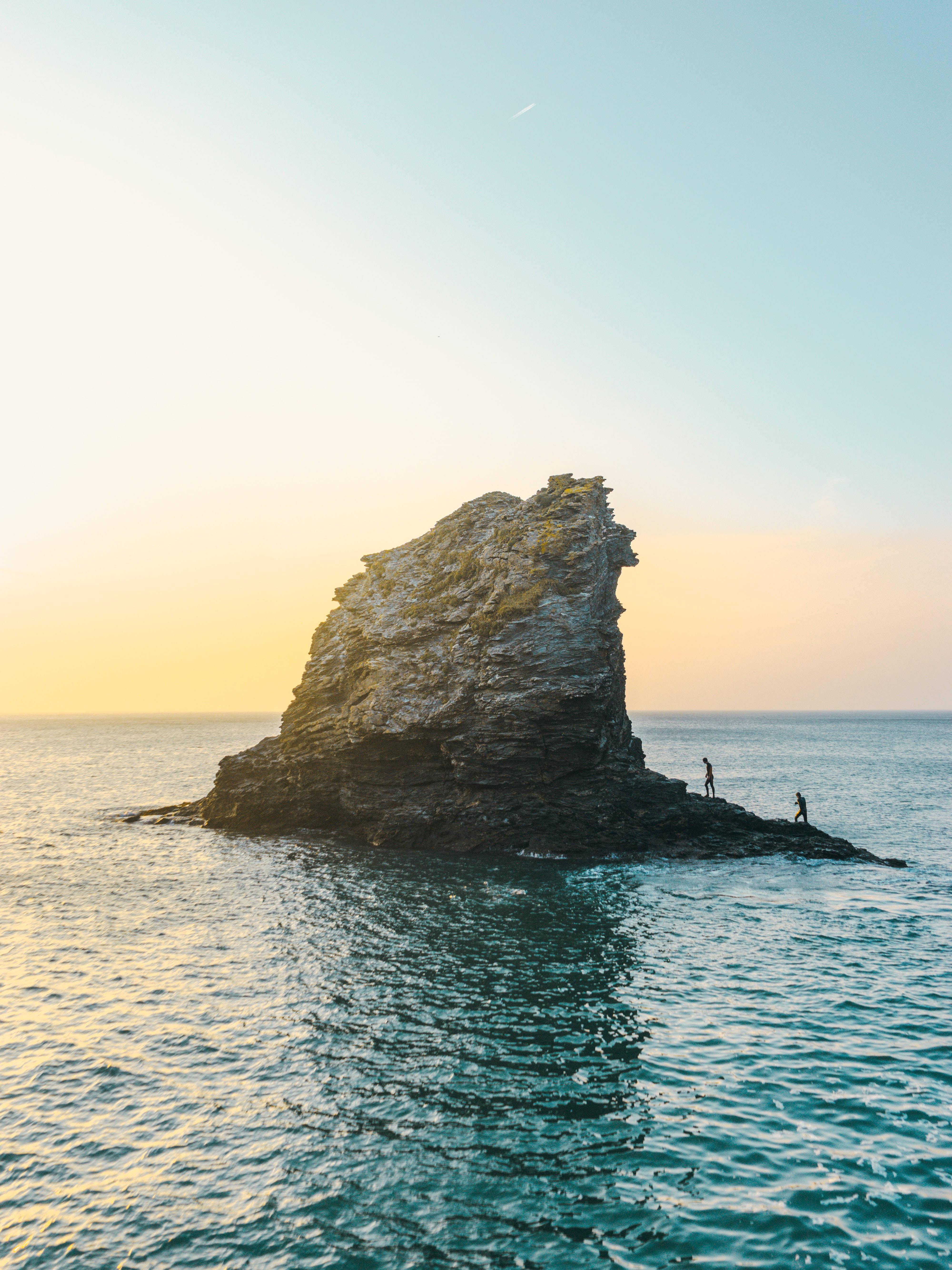 島嶼 桌布 壁紙 — 兩個小人影站在崎嶇的海蝕柱頂，金色夕陽光照耀著平靜的海洋和天空。