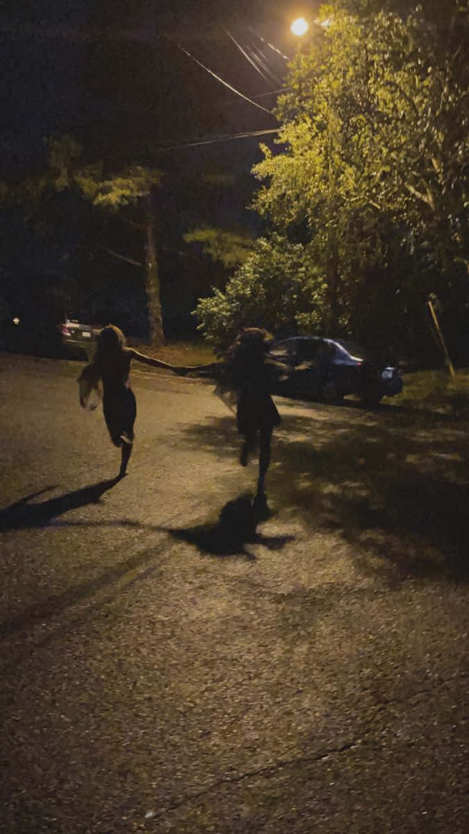 情侶 桌布 壁紙 — 兩個小孩手牽手在夜晚昏暗的街道上，在發光的街燈下奔跑。