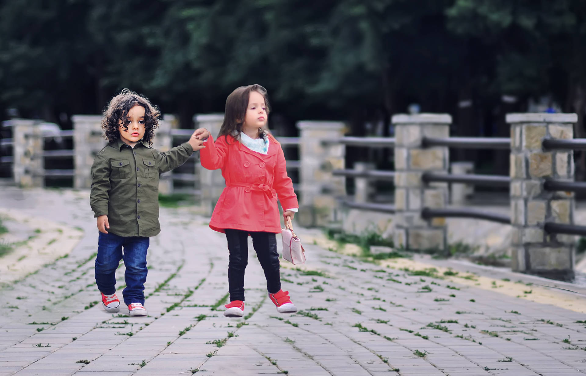 兩個小孩手牽手在公園的石徑上行走。