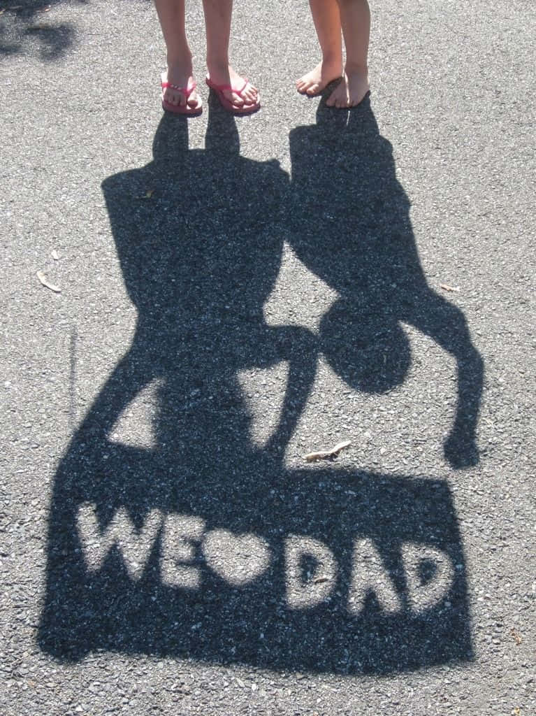 Fathers Day 桌布 壁紙 — 兩個小孩的影子在人行道上用粉筆拼出「WE ❤️ DAD」，他們的腳站在附近。