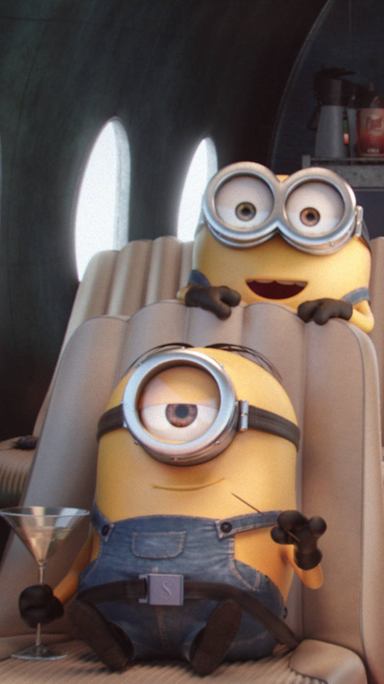Minion Phone 桌布 壁紙 — 兩個小小兵在豪華噴射機座位上放鬆，一個啜飲馬丁尼，另一個戴著超大護目鏡咧嘴笑。