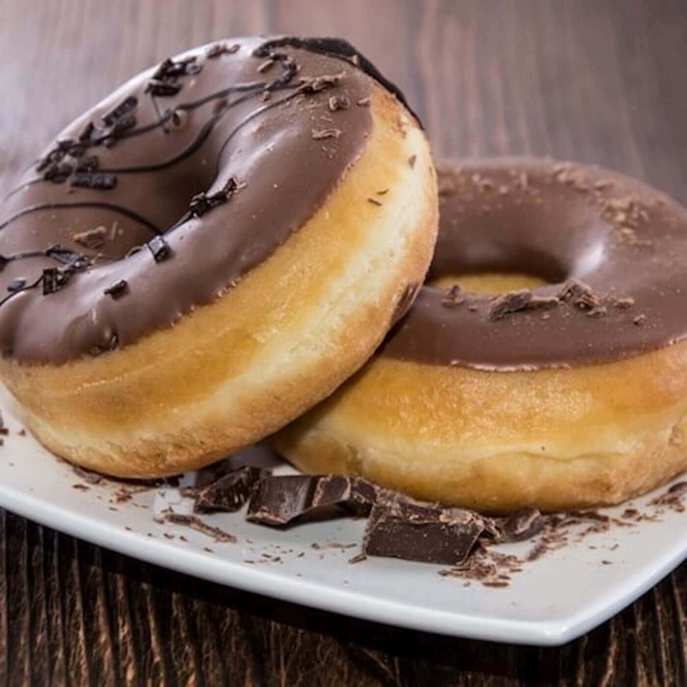Donut 桌布 壁紙 — 兩個巧克力釉面甜甜圈配上巧克力碎片，放在深色木質表面上的白色盤子上。