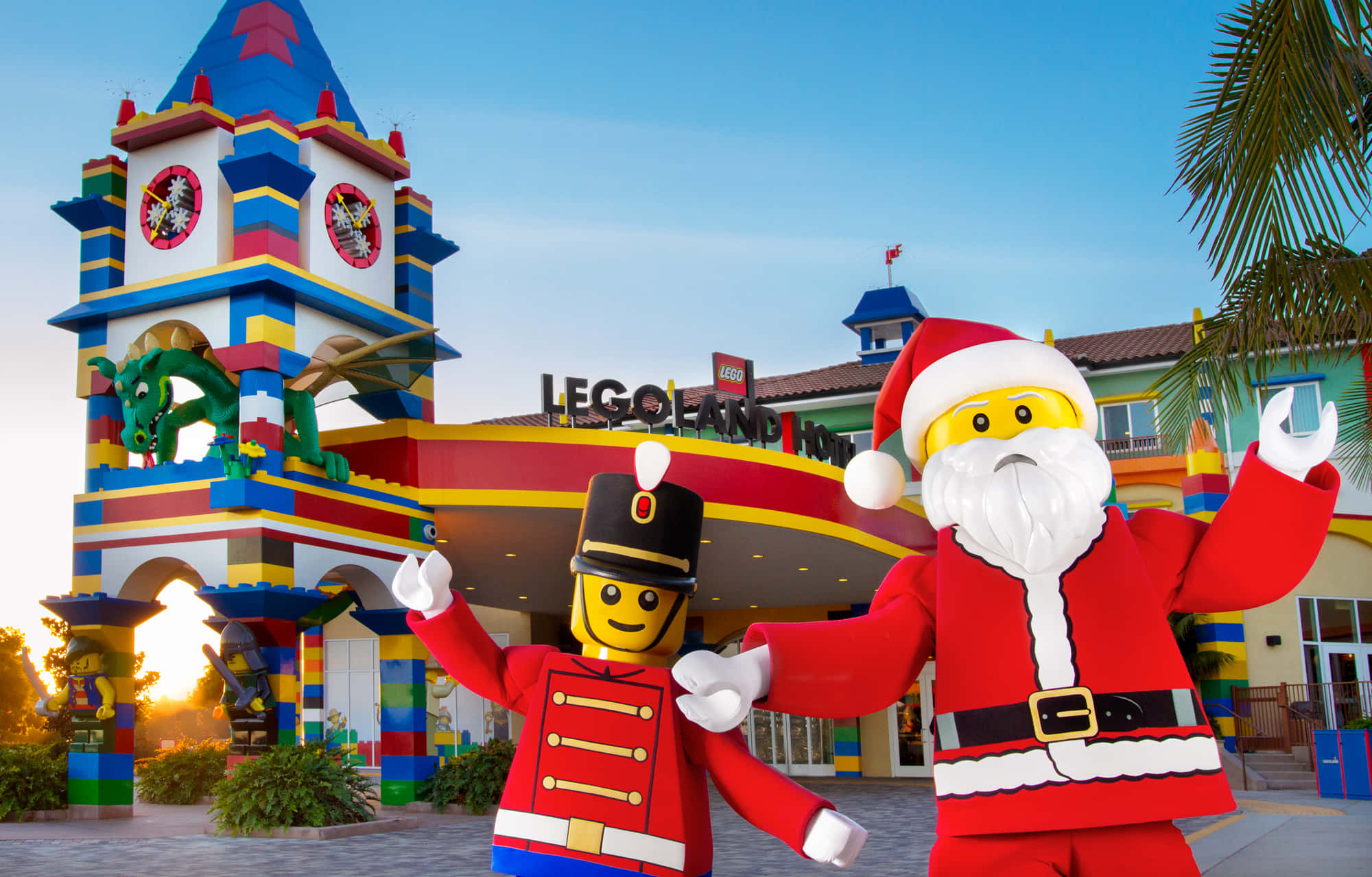 Legoland 桌布 壁紙 — 兩個巨型LEGO公仔，一個士兵和聖誕老人，在日落時分愉快地站在色彩繽紛的LEGO主題遊樂園入口前。