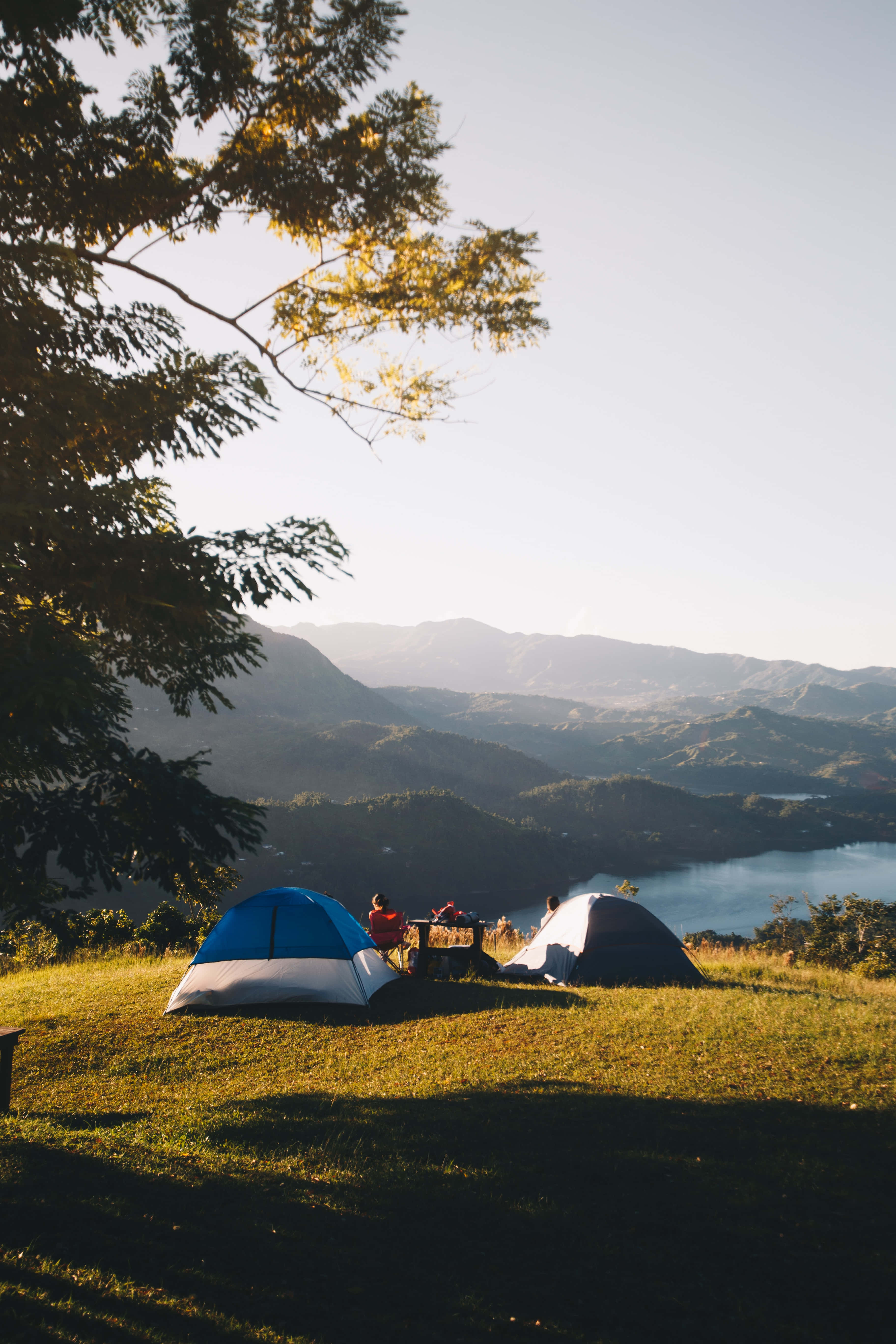 Camping 桌布 壁紙 — 兩個帳篷坐落於一個草坡上，俯瞰著一個寧靜的湖泊和沐浴在金色晨光中的遠山。