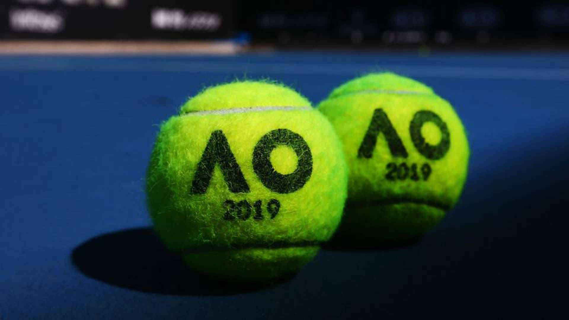 Australian Open 桌布 壁紙 — 兩個帶有AO 2019標誌的亮黃色網球，在聚焦燈光下放置在深藍色球場表面上。