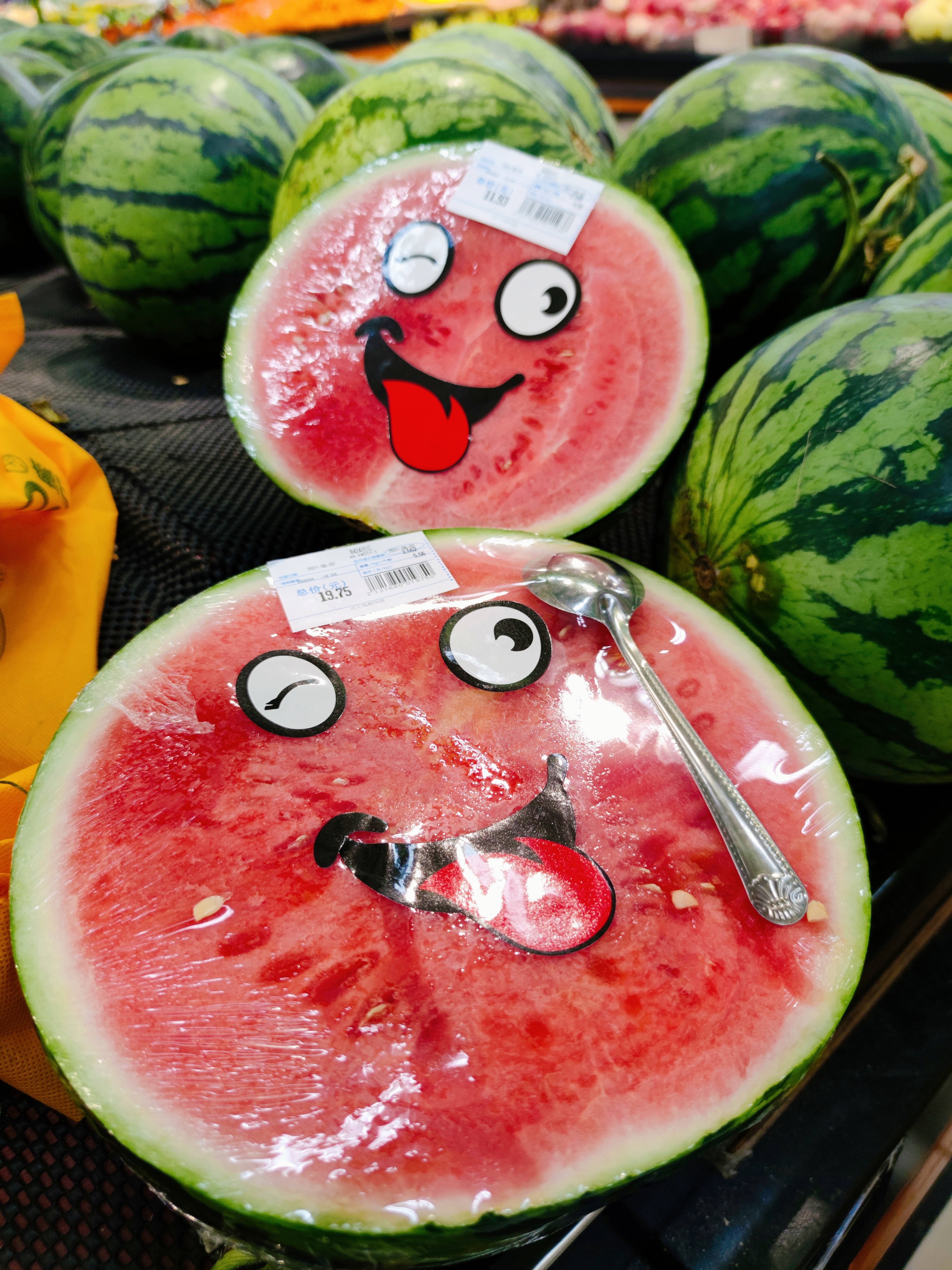 Watermelon 桌布 壁紙 — 兩個帶有卡通面孔和伸出舌頭的西瓜半邊，坐在雜貨店裡的整個西瓜中。