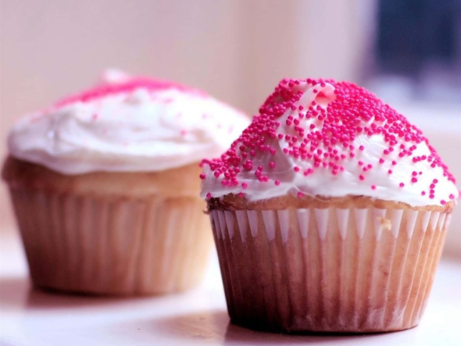 Pink Cupcakes 桌布 壁紙 — 兩個帶有白色糖霜和粉紅色糖粒的杯子蛋糕緊靠在一起，一個清晰對焦，另一個柔和模糊。
