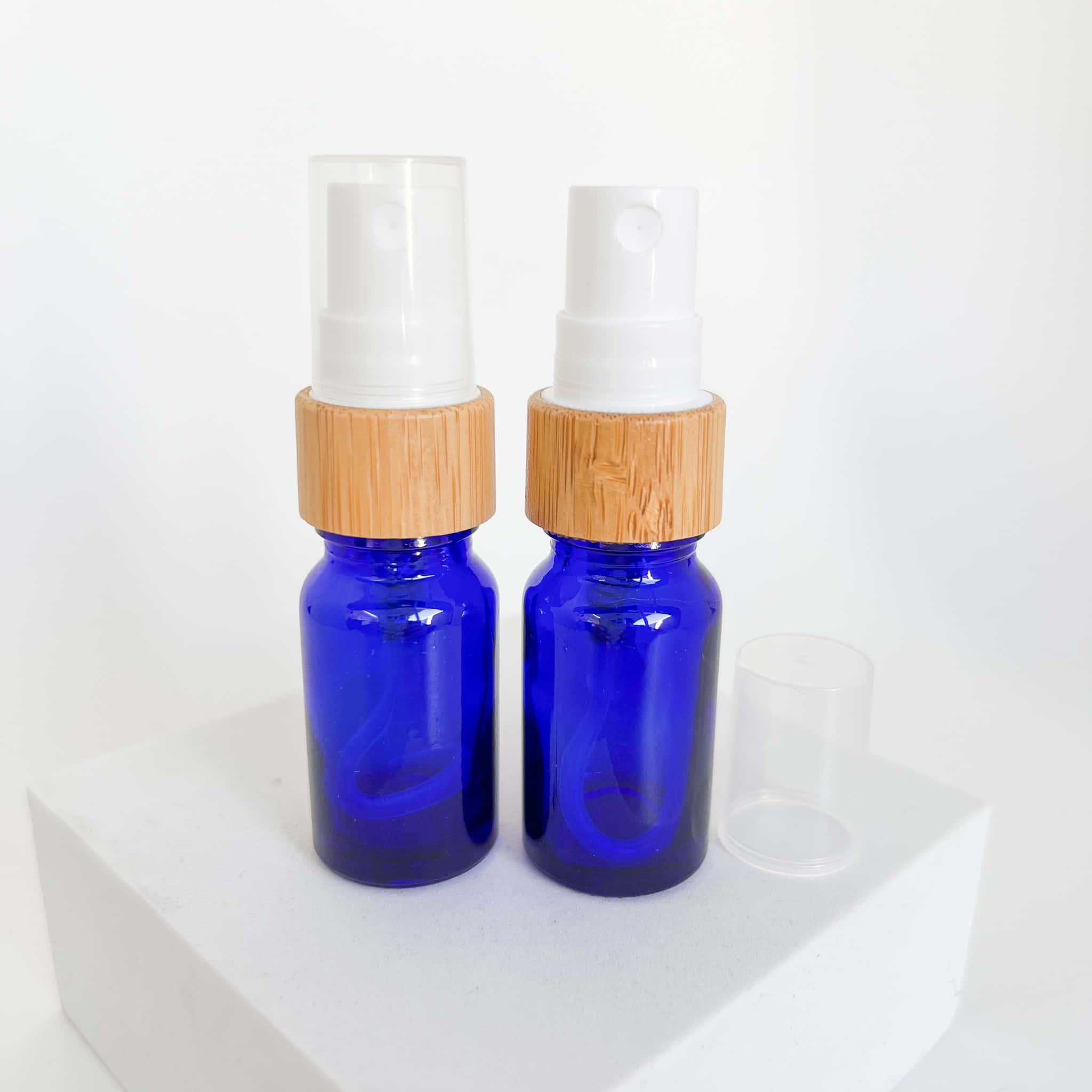 Cobalt Blue 桌布 壁紙 — 兩個帶竹蓋的鈷藍色玻璃噴霧瓶整齊地放在白色塊上，背景為純白色。