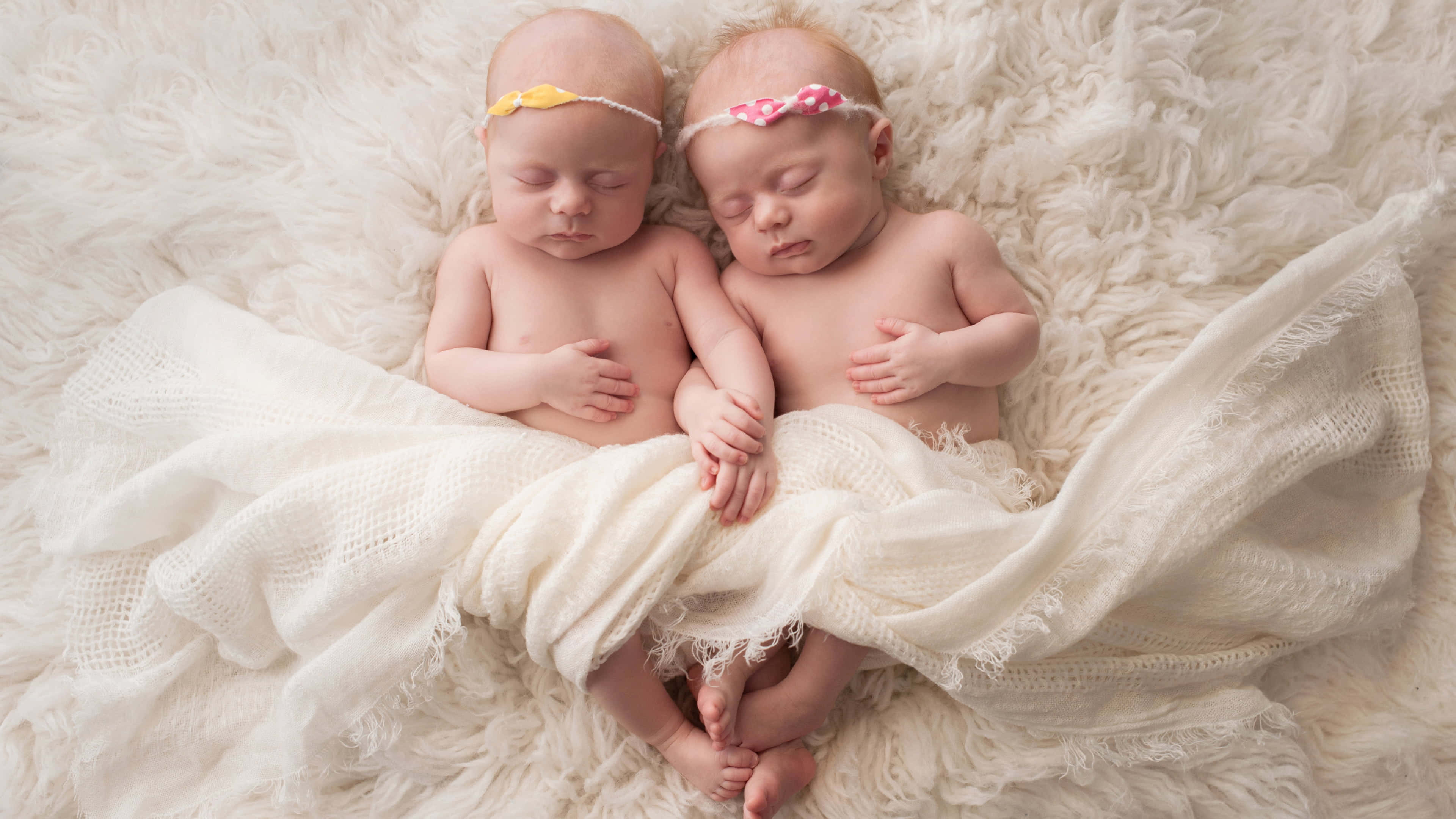 Cute Babies 桌布 壁紙 — 兩個平靜的新生雙胞胎並排睡在 fluffy 白色地毯上，戴著小頭帶。
