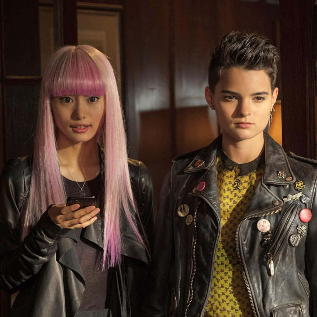 Negasonic Teenage Warhead 桌布 壁紙 — 兩個年輕人留著大膽的粉紅色頭髮，穿著皮夾克，站在室內，其中一人拿著手機，兩人都表情嚴肅。