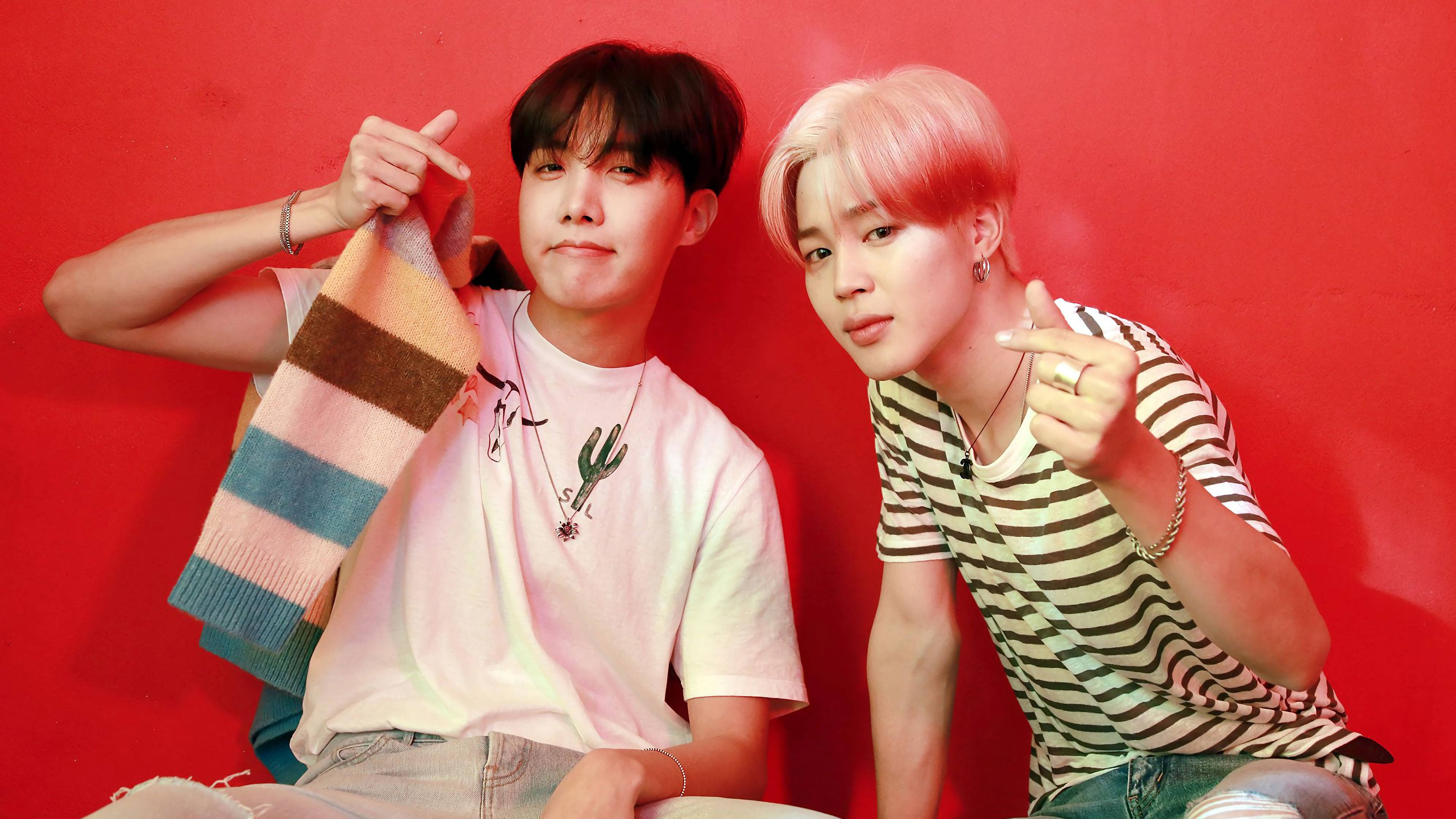 jhope 桌布 壁紙 — 兩個年輕男子在鮮紅色的牆前擺出俏皮的姿勢，一個拿著條紋圍巾，另一個指著相機。