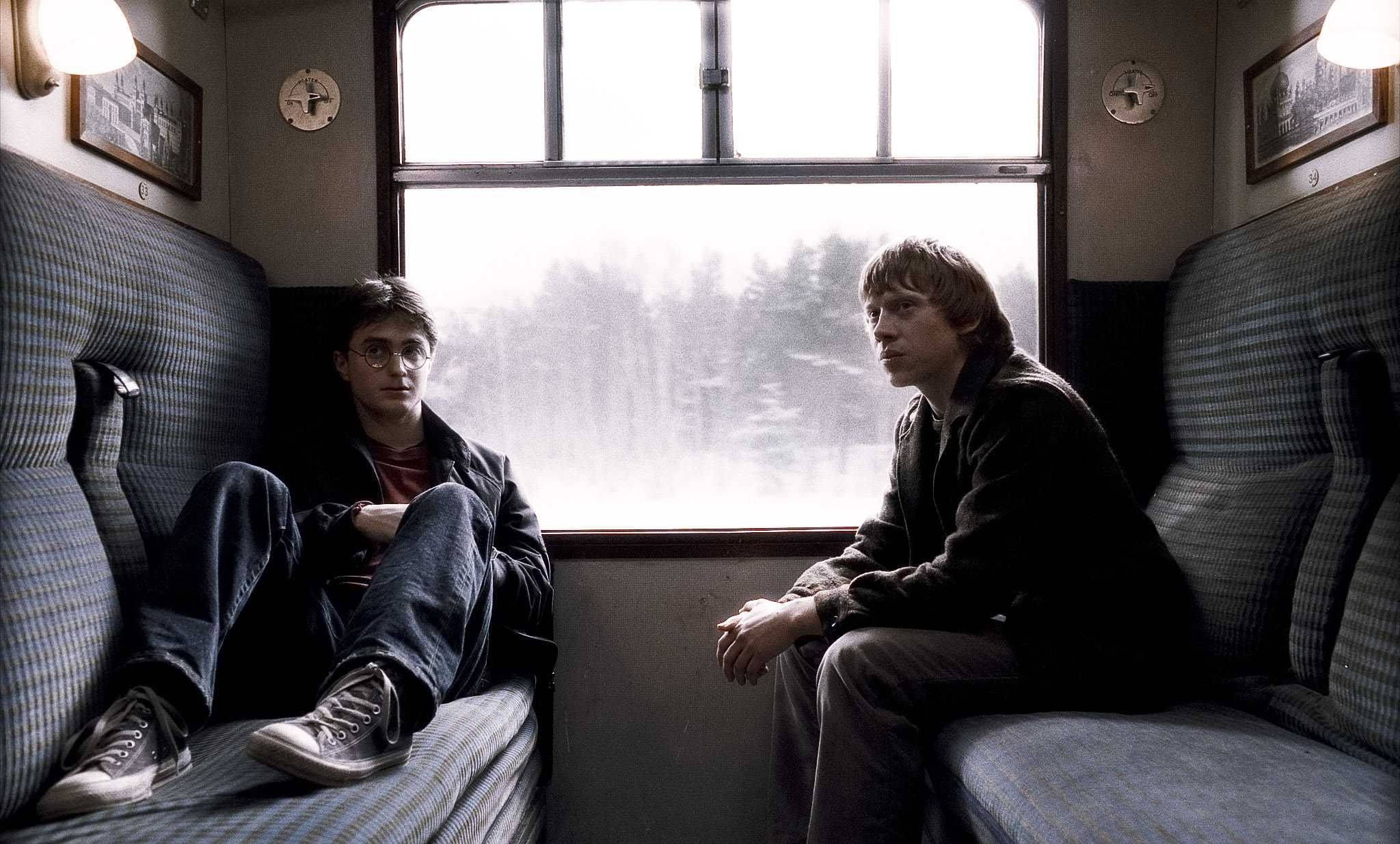 Ron Weasley 桌布 壁紙 — 兩個年輕男子面對面坐在火車長椅上，透過霧氣濛濛的窗戶望向森林。