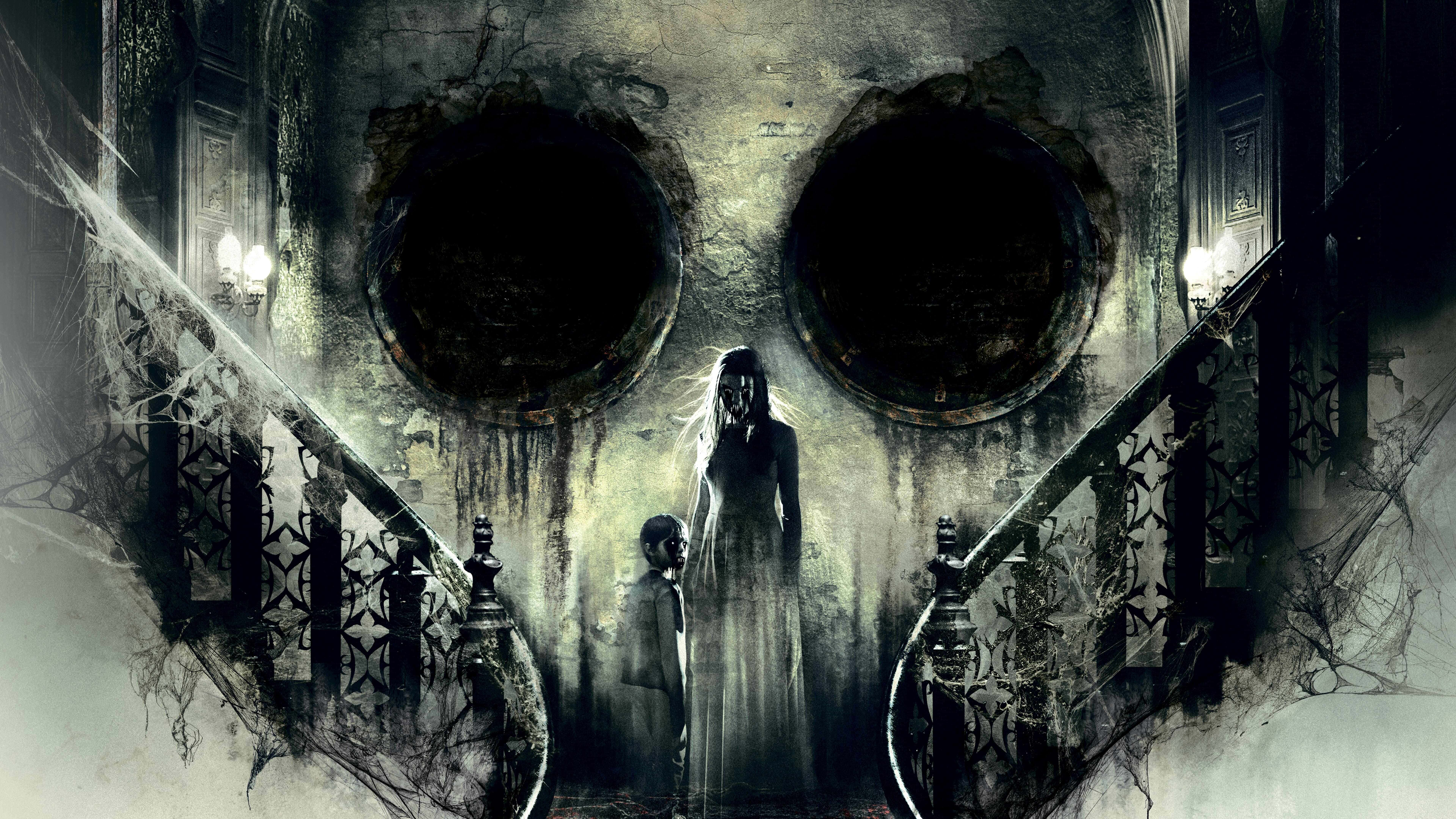 Horror Masks 桌布 壁紙 — 兩個幽靈般的身影站在一座破敗大宅中宏偉樓梯的底部，上方是一幅巨大的骷髏壁畫。