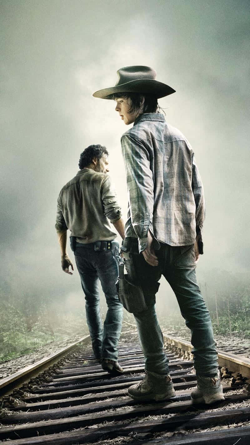 The Walking Dead iPhone 桌布 壁紙 — 兩個強壯的男人在朦朧的天空下沿著霧氣瀰漫的鐵軌走遠。
