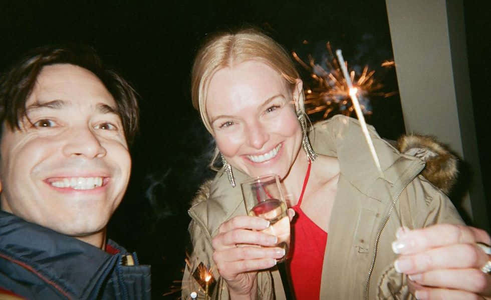 Justin Long 桌布 壁紙 — 兩個微笑的人在夜間戶外節日環境中手持煙火棒和香檳慶祝。