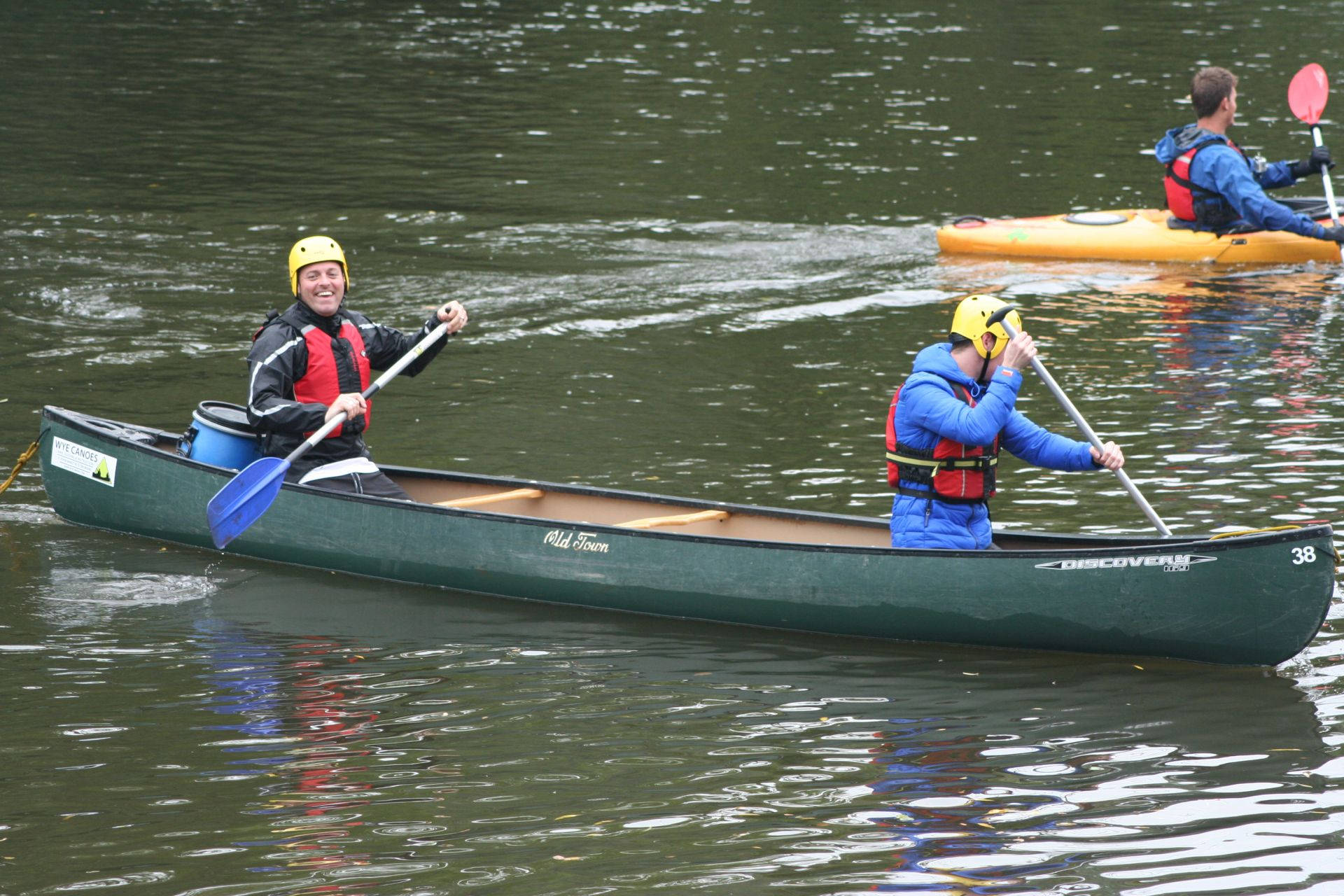 Rowing 桌布 壁紙 — 兩個微笑的人在平靜的水面上划綠色獨木舟，另一個皮划艇手跟在後面。
