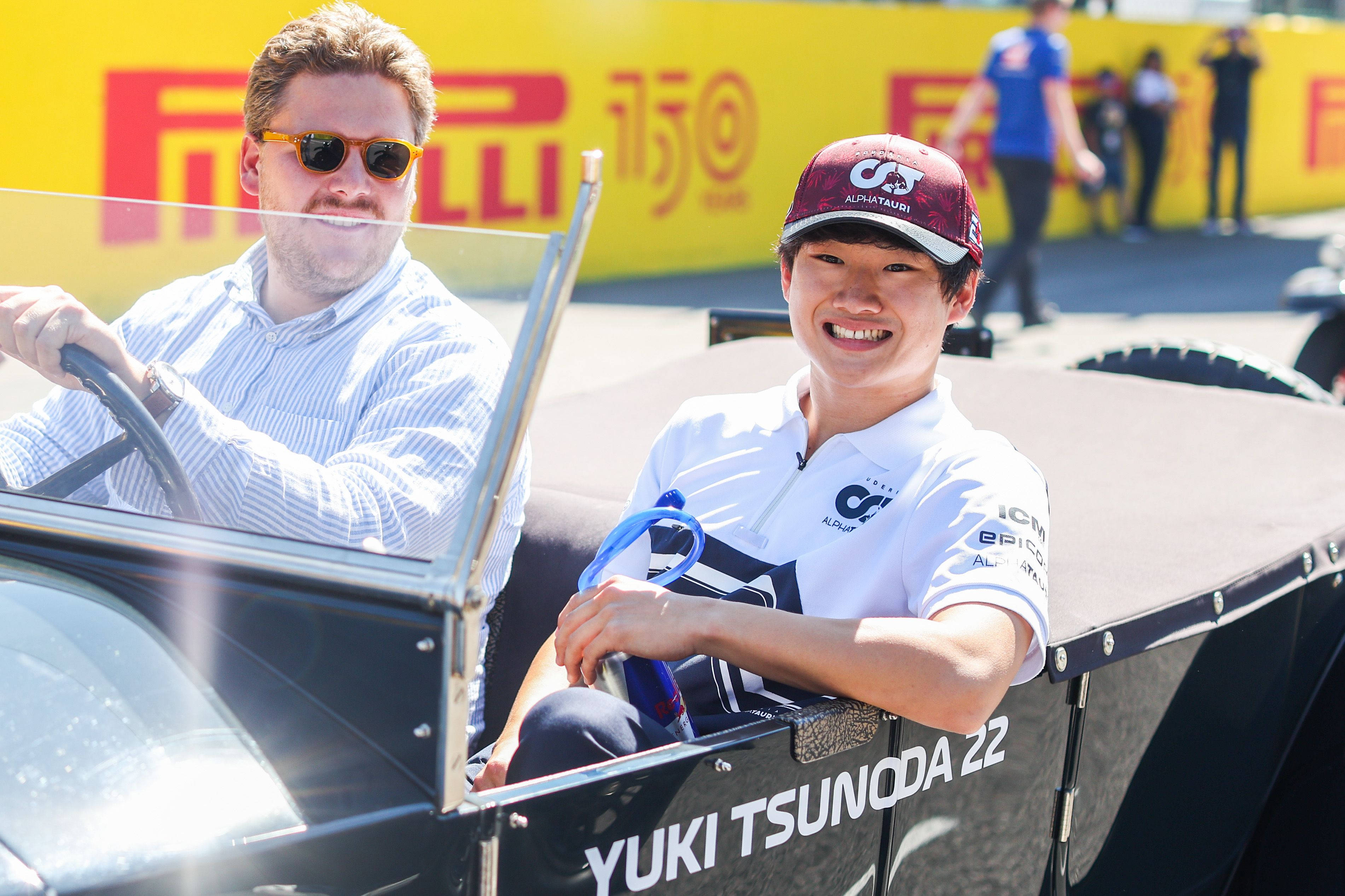 Smile 桌布 壁紙 — 兩個微笑的人坐在一輛黑色敞篷賽車上，車側有「YUKI TSUNODA 22」字樣，在明亮的陽光下戶外擺姿勢。