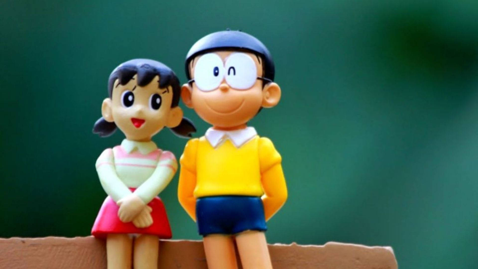 shizuka doraemon 桌布 壁紙 — 兩個微笑的動漫風格哆啦A夢和靜香公仔並排坐在木製架子上，背景是柔和的綠色。