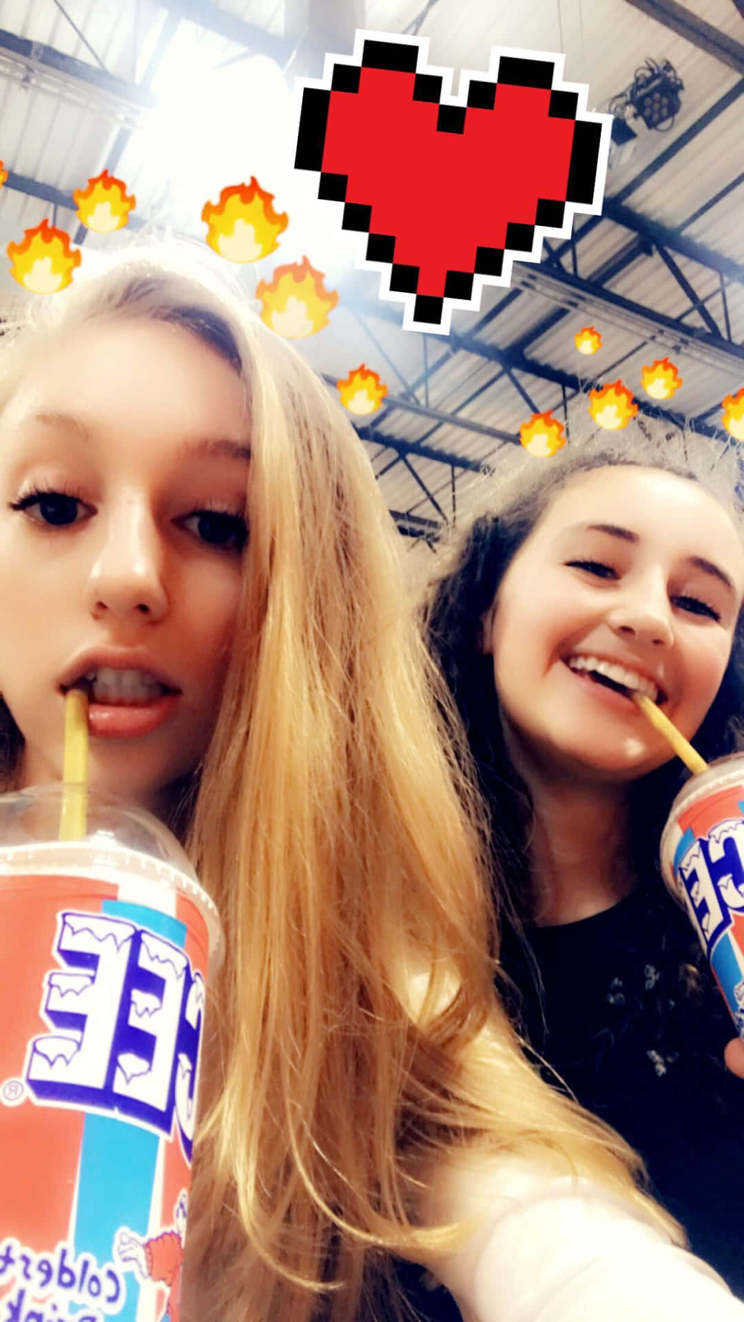 Snapchat 桌布 壁紙 — 兩個微笑的女孩在高天花板下啜飲飲料，上面疊加了像素心形和火焰濾鏡。