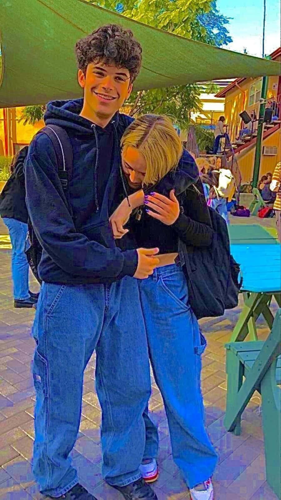 Cute Boyfriend 桌布 壁紙 — 兩個微笑的年輕人在陽光明媚的戶外聚會中，在綠色遮陽篷下溫暖地擁抱。