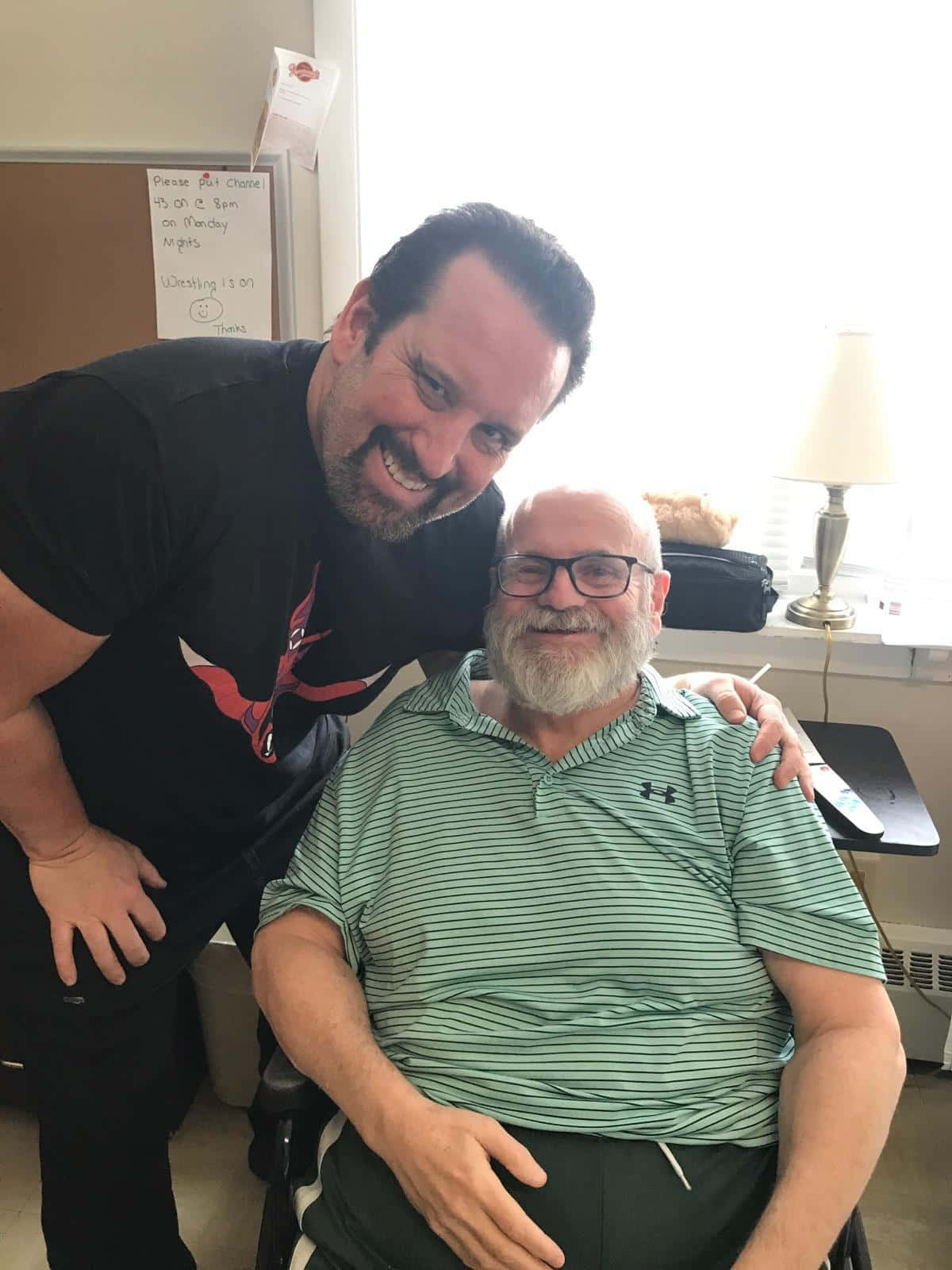 WWE 桌布 壁紙 — 兩個微笑的男人，其中一個靠在另一個身上，在一個明亮的房間裡，有一張輪椅和一盞燈。