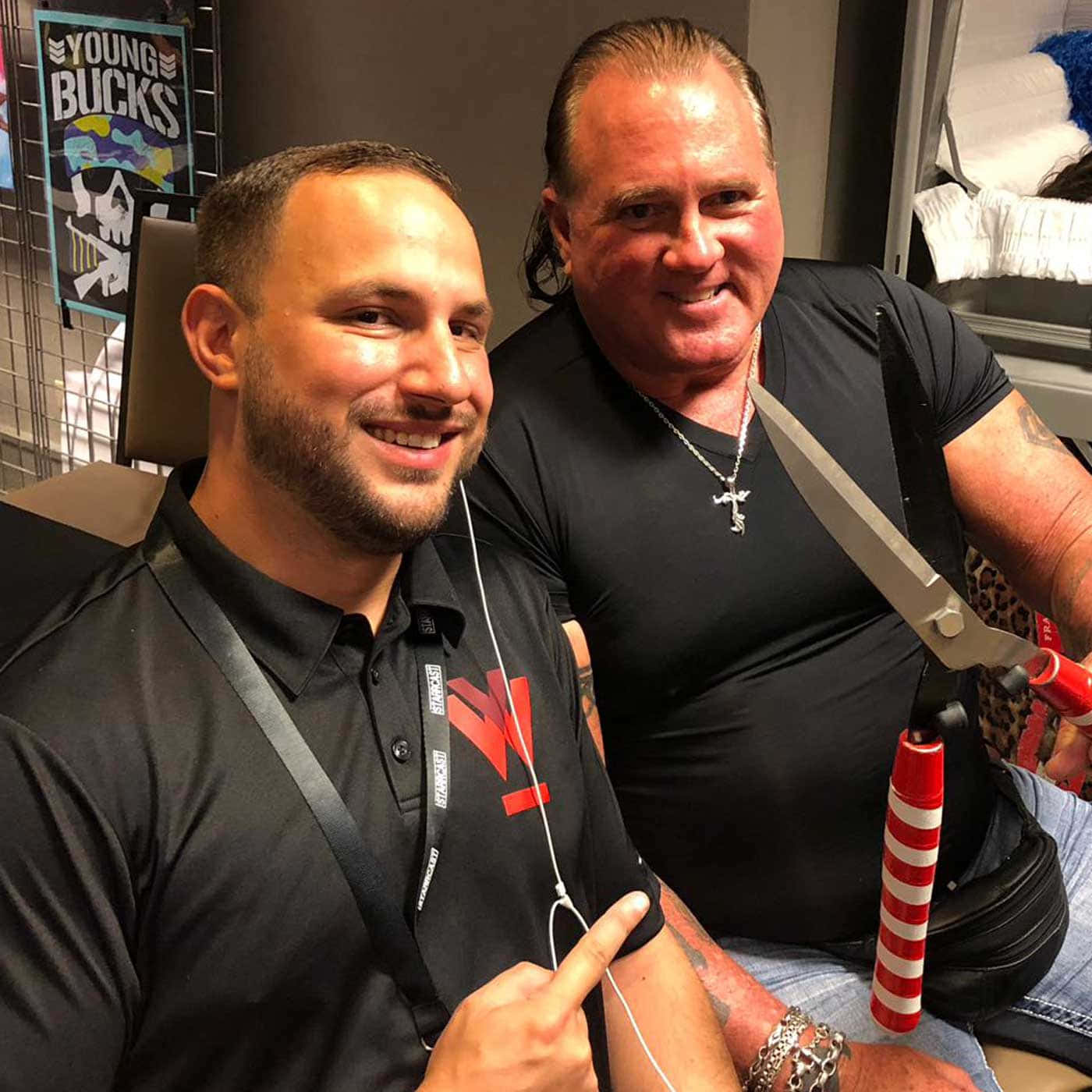 Brutus Beefcake 桌布 壁紙 — 兩個微笑的男人在室內擺姿勢，一個拿著巨型剪刀，另一個用耳塞指著自己的手臂。