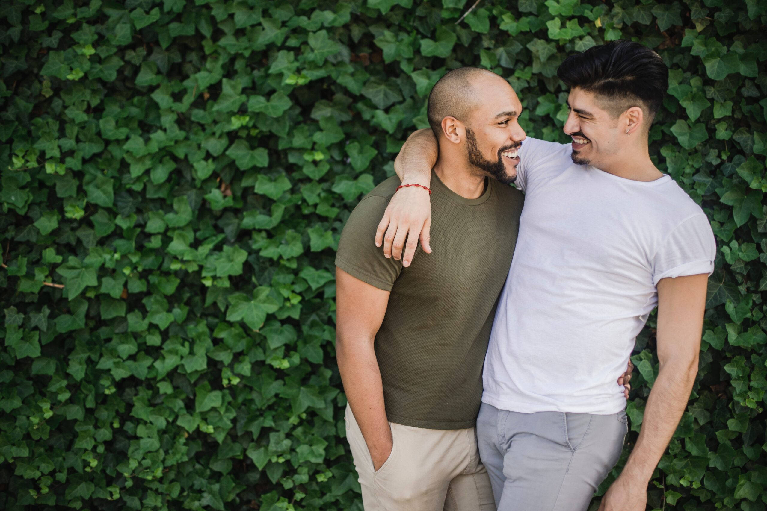 gay love 桌布 壁紙 — 兩個微笑的男人在明亮的日光下，在茂密的綠色常春藤牆前熱情擁抱。