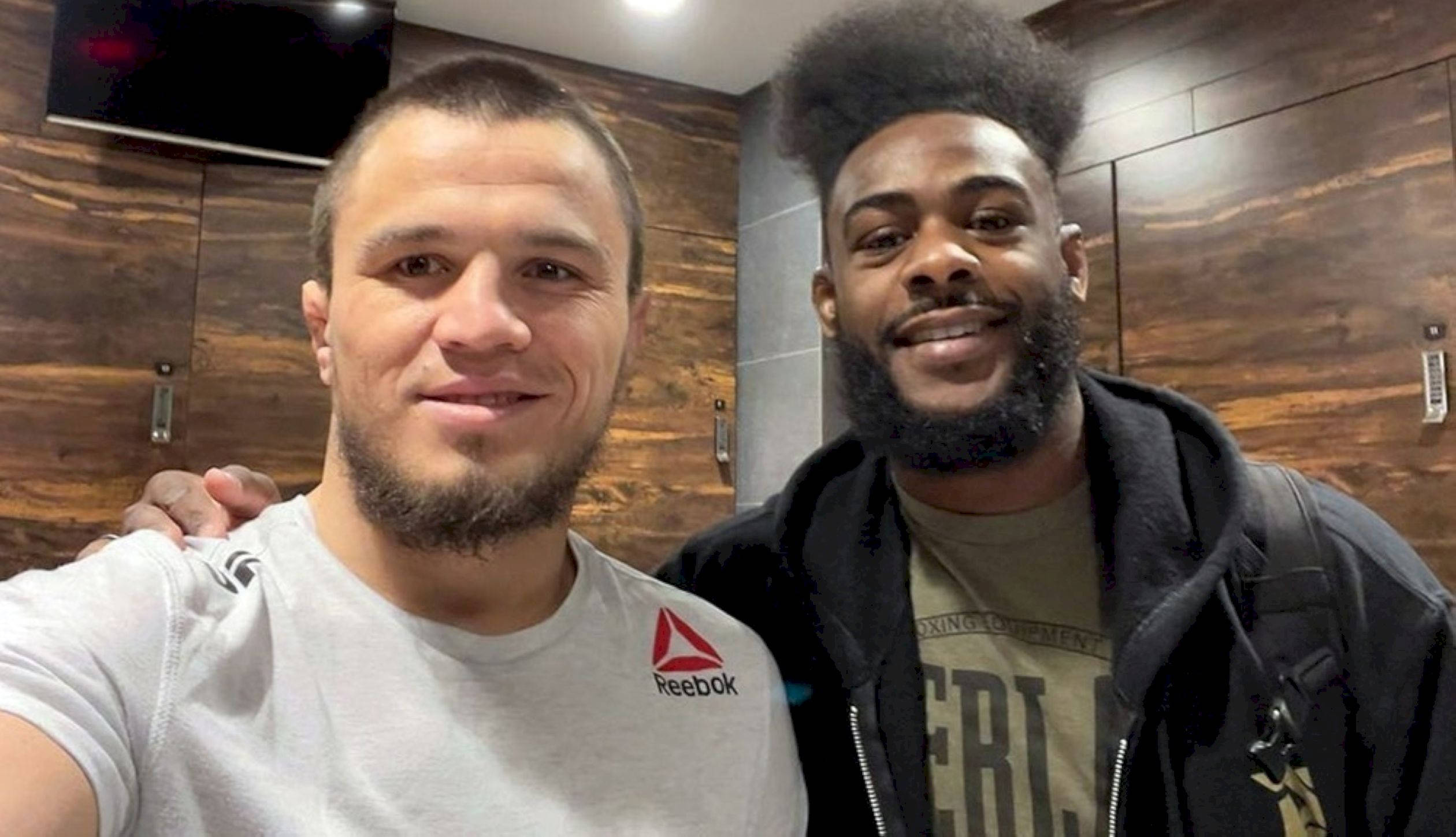 UFC 桌布 壁紙 — 兩個微笑的男人在木質鑲板的更衣室裡自拍，身後牆上掛著電視。