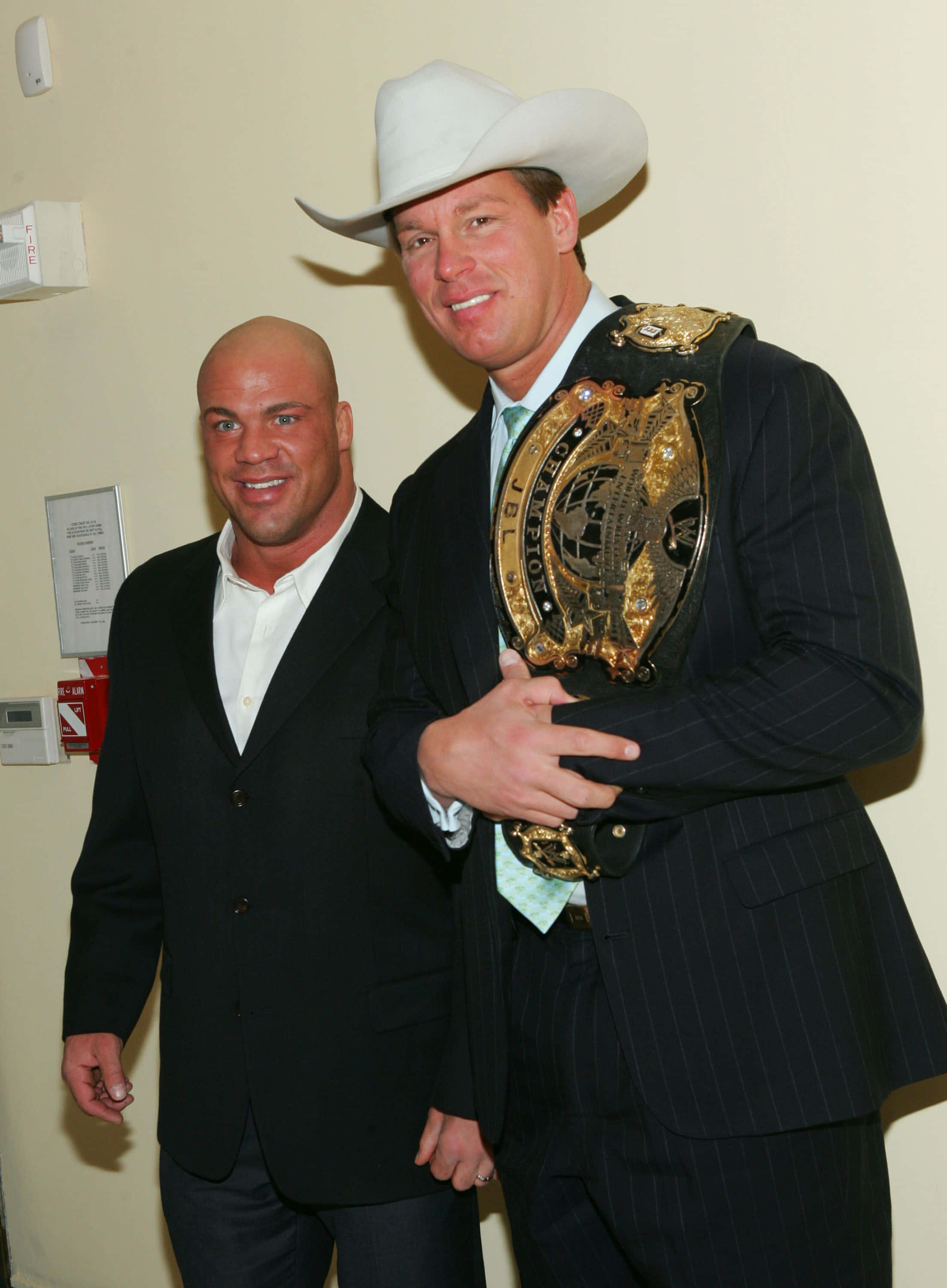 WWE 桌布 壁紙 — 兩個微笑的男人穿著西裝，其中一個戴著白色牛仔帽，室內拿著金色冠軍腰帶。