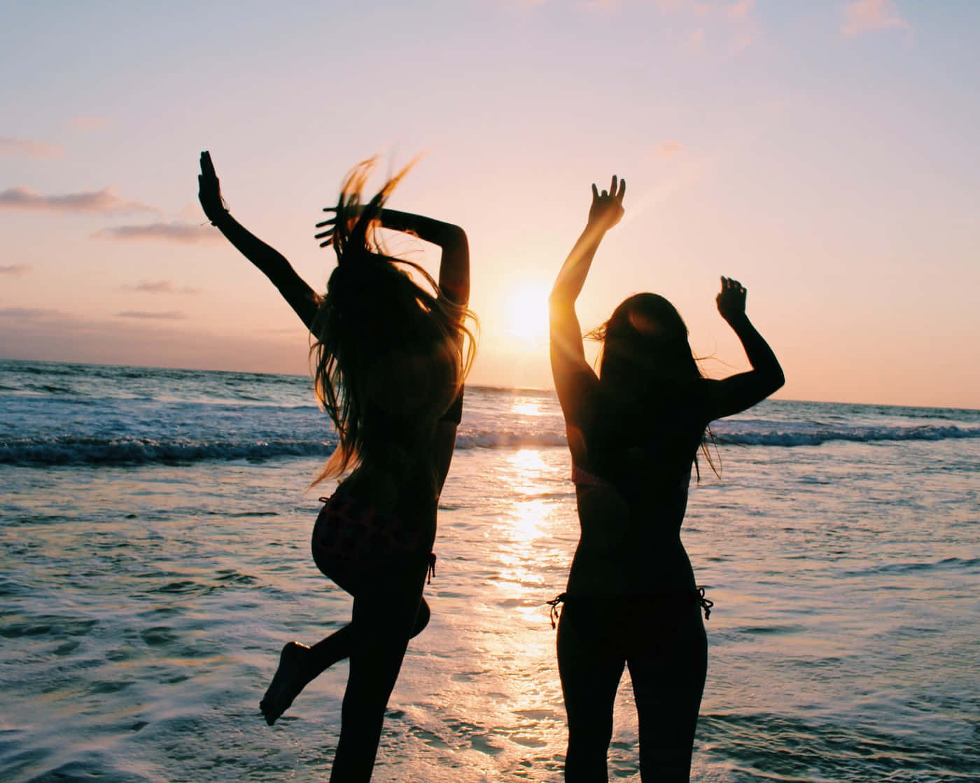 Friends 桌布 壁紙 — 兩個快樂的剪影女孩在日落時分於閃閃發光的海邊跳躍並舉起雙臂。