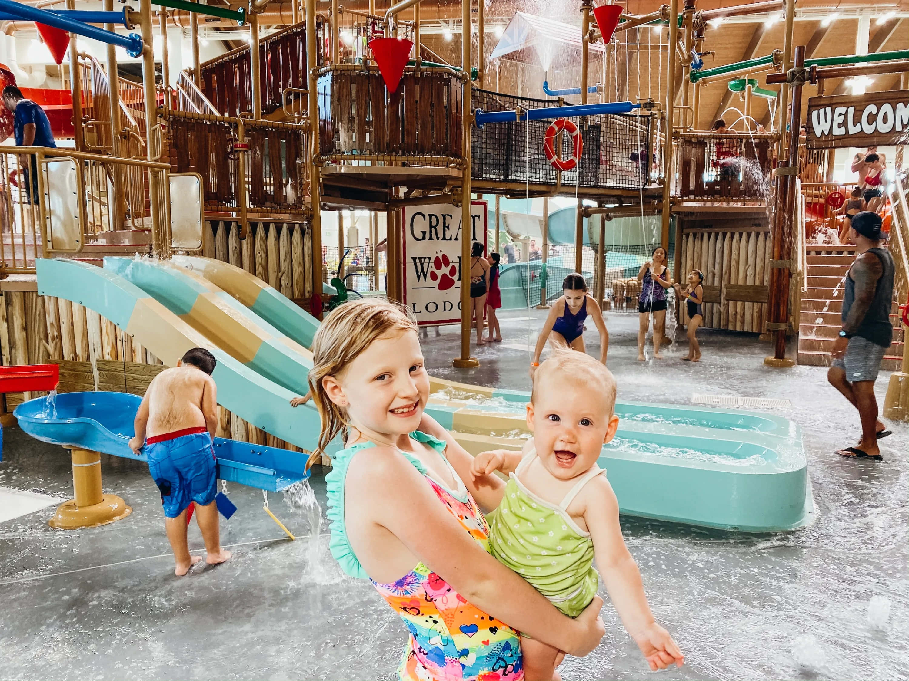 great wolf lodge 桌布 壁紙 — 兩個快樂的孩子在一個熱鬧的室內水上樂園裡大笑，那裡有色彩繽紛的滑梯和飛濺的泳池。