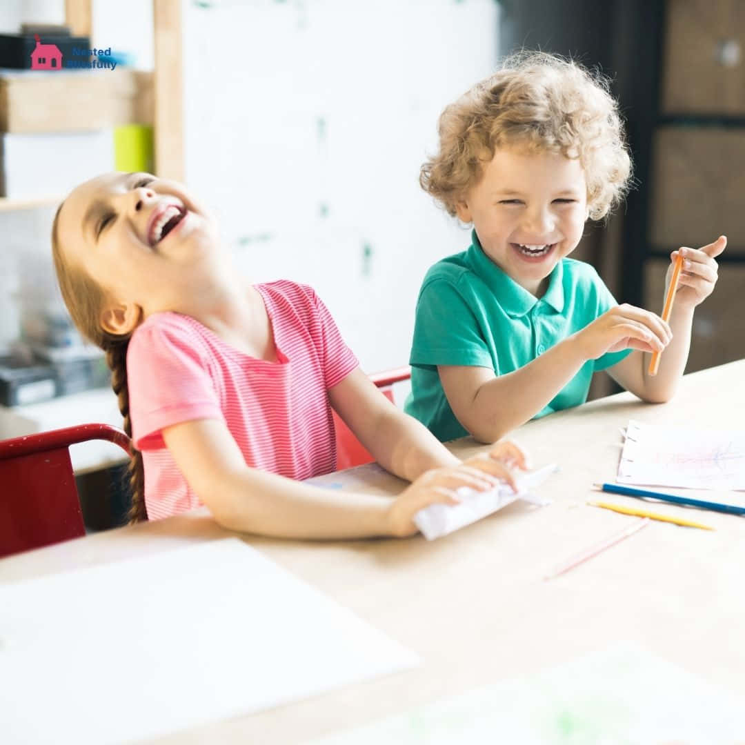 小孩動圖 桌布 壁紙 — 兩個快樂的孩子坐在明亮的教室裡的木桌前，面前擺放著美術用品，開懷大笑。