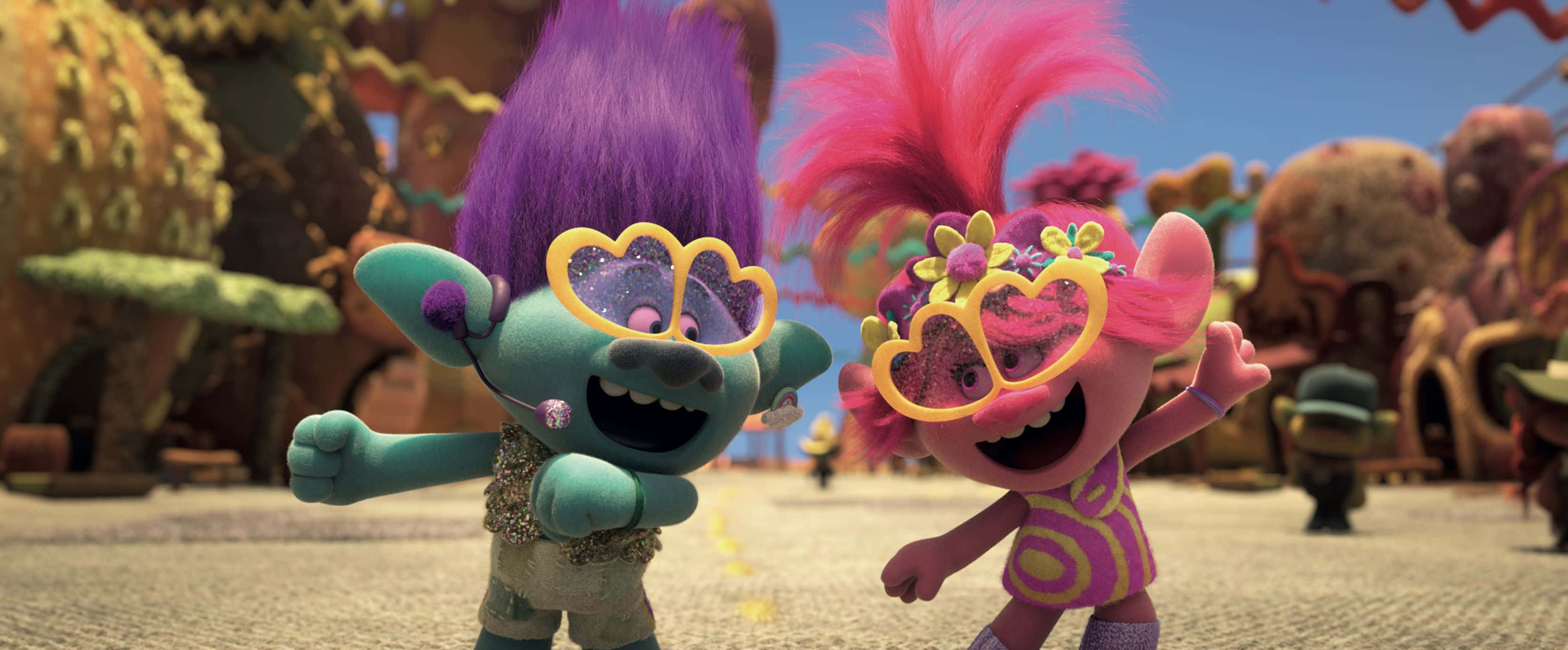 Trolls World Tour 桌布 壁紙 — 兩個快樂的巨魔角色，擁有充滿活力的紫色和粉紅色頭髮，在晴朗的藍天下，在色彩繽紛的幻想村莊中充滿活力地跳舞。