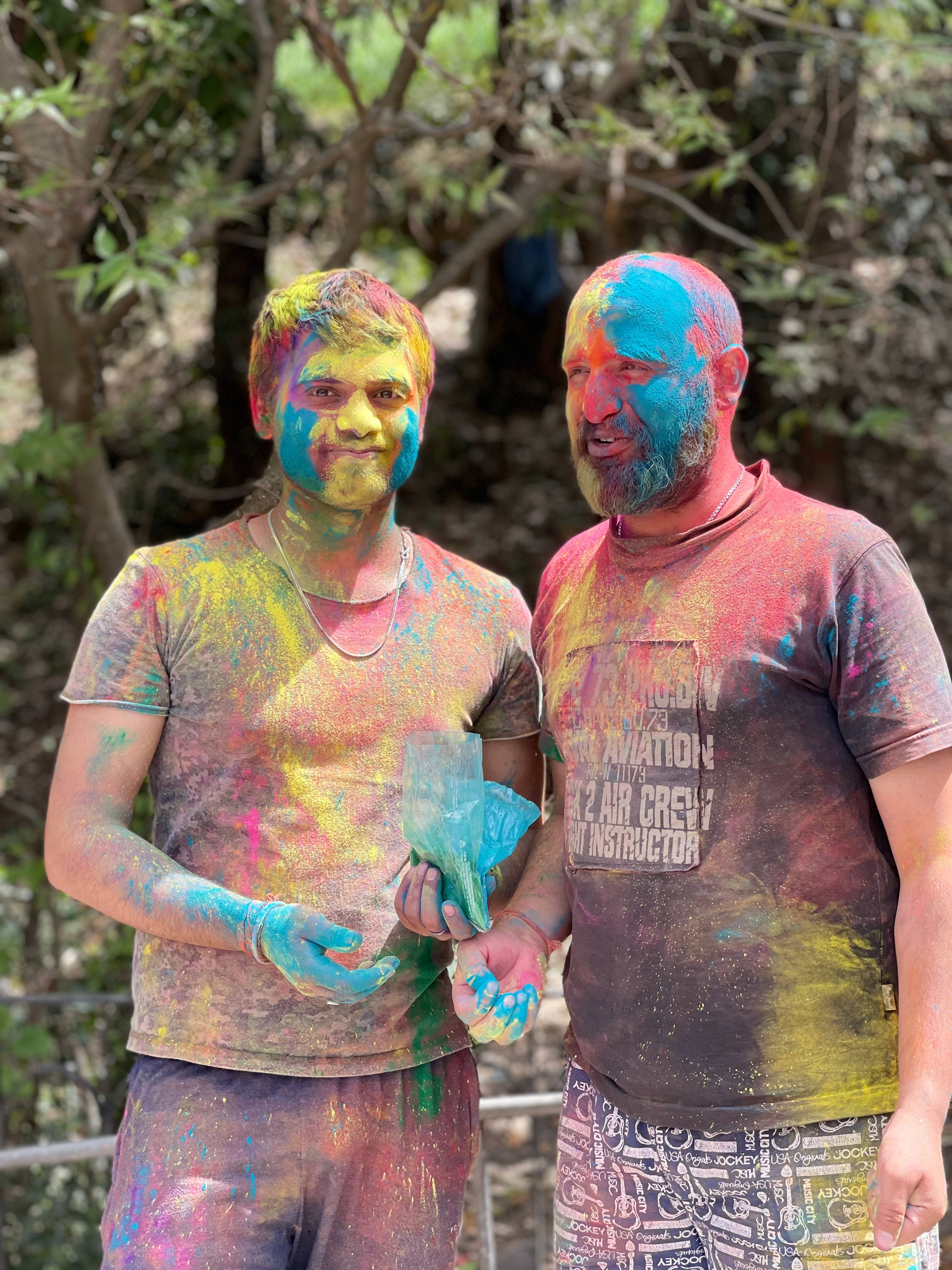 Holi 桌布 壁紙 — 兩個快樂的男人身上佈滿鮮豔的粉末顏色，在陽光明媚的樹林地區微笑站立。